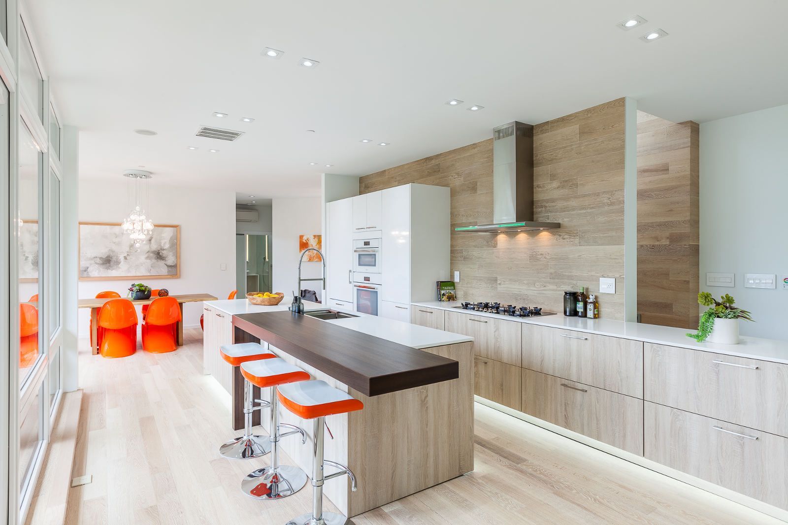 A kitchen with a large island and stools and a dining room in the background.