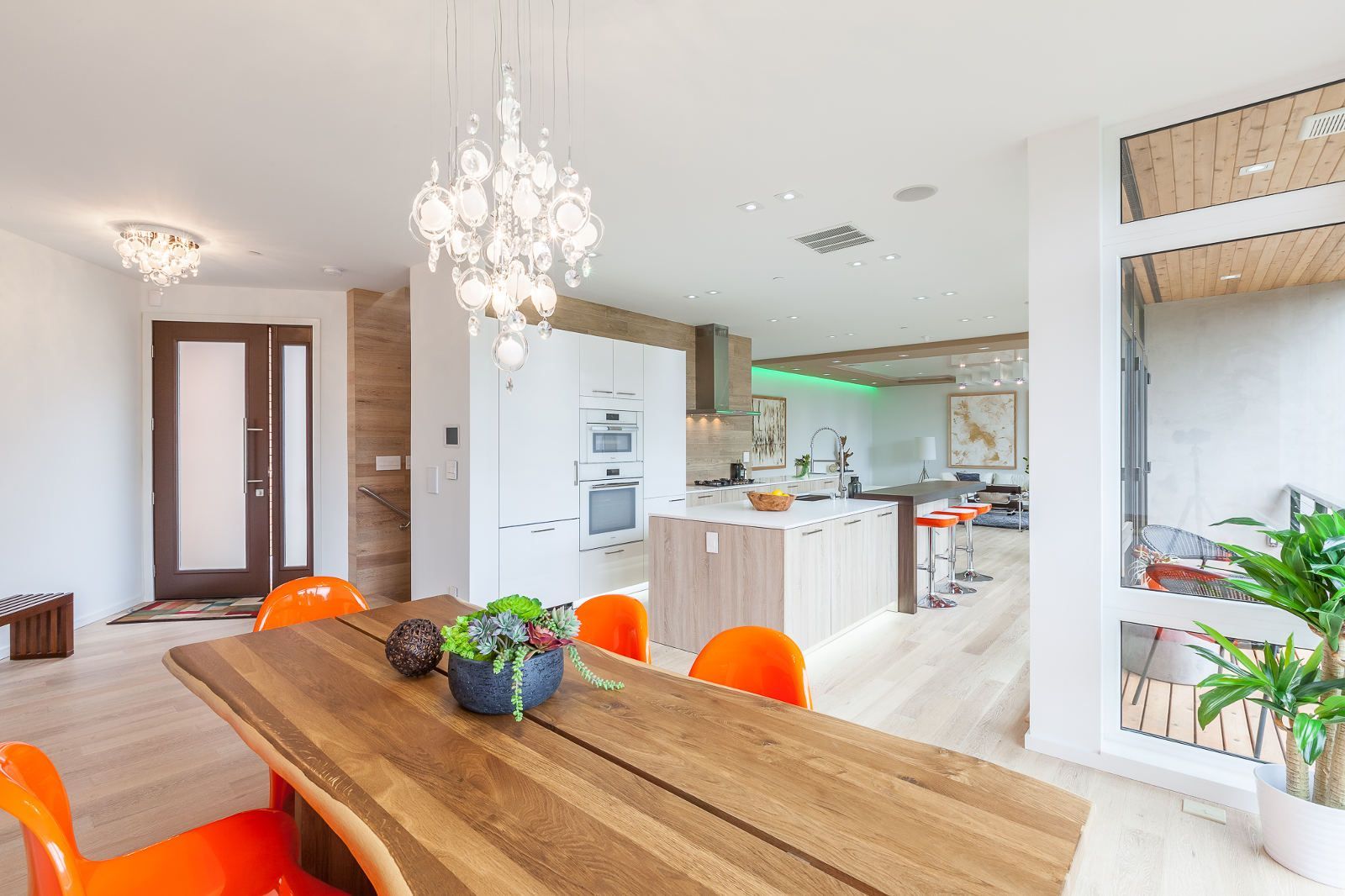 A dining room with a wooden table and orange chairs and a chandelier hanging from the ceiling.