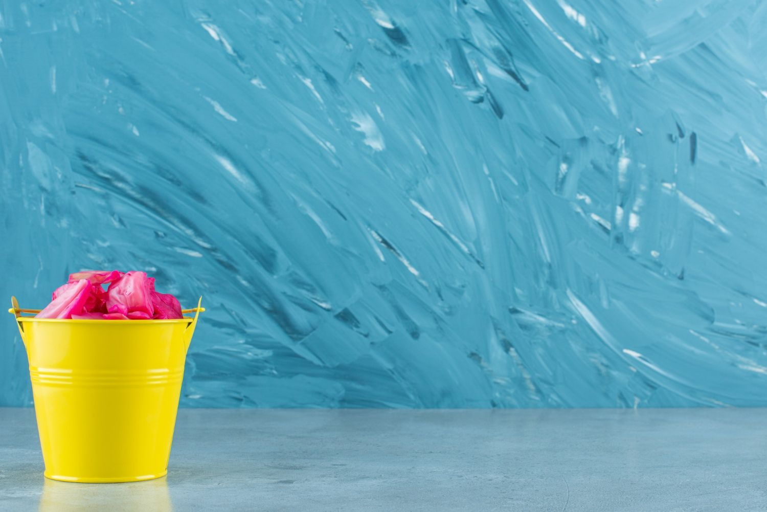 A yellow bucket filled with pink flowers on a blue background.