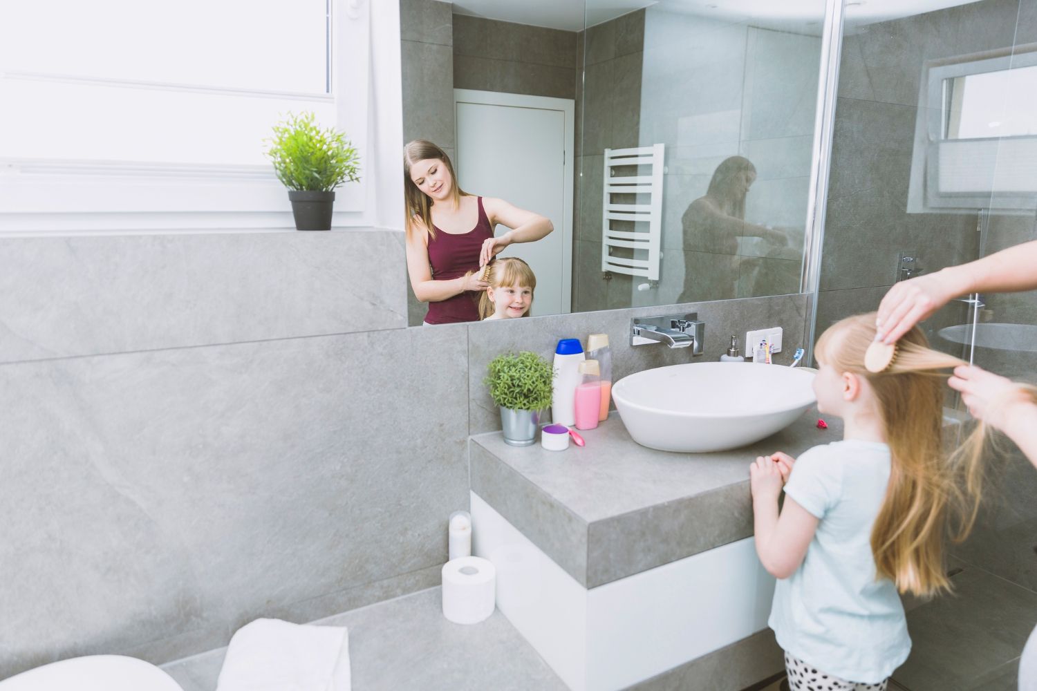 A woman is brushing a little girl 's hair in a bathroom.