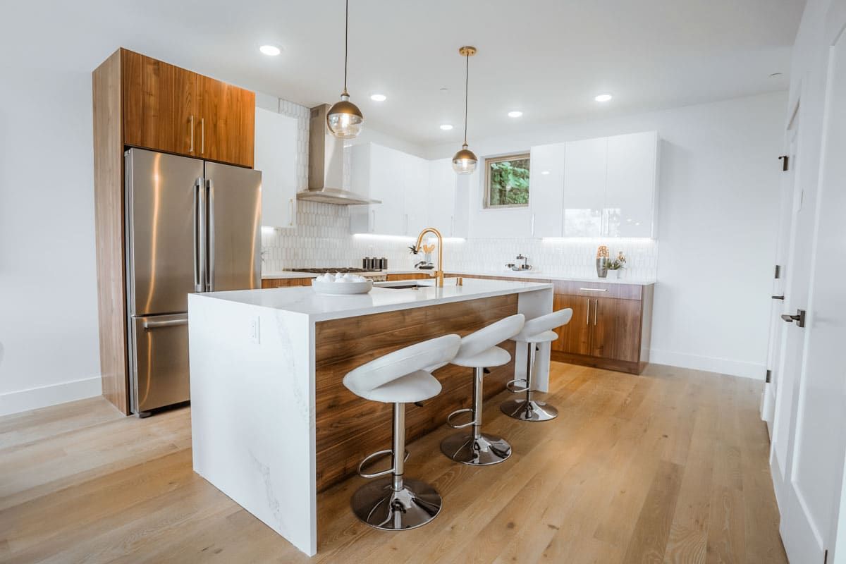 A kitchen with a large island , stools , a refrigerator and a sink.