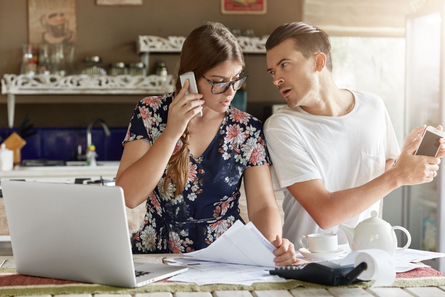 A man and a woman are sitting at a table with a laptop and a cell phone.