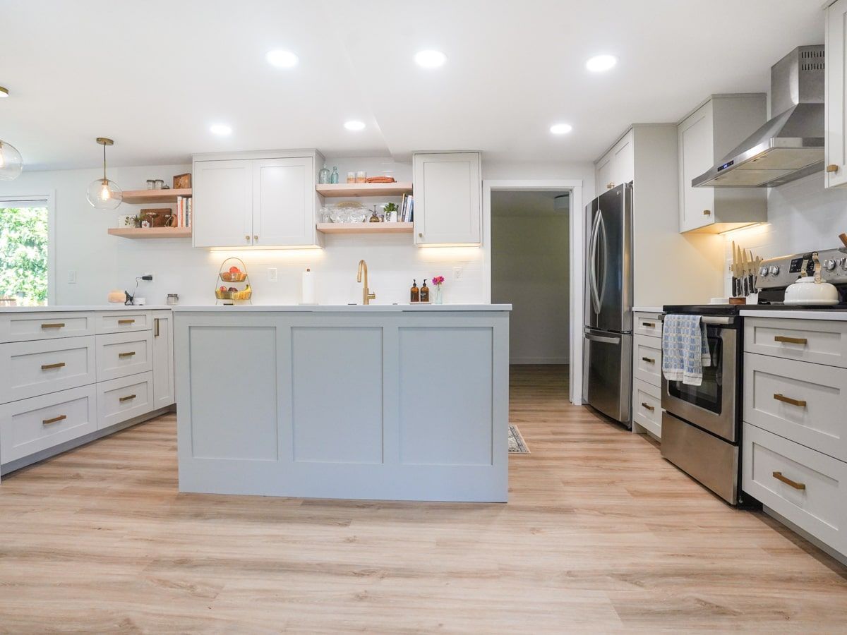 A kitchen with white cabinets and stainless steel appliances and a large island in the middle.