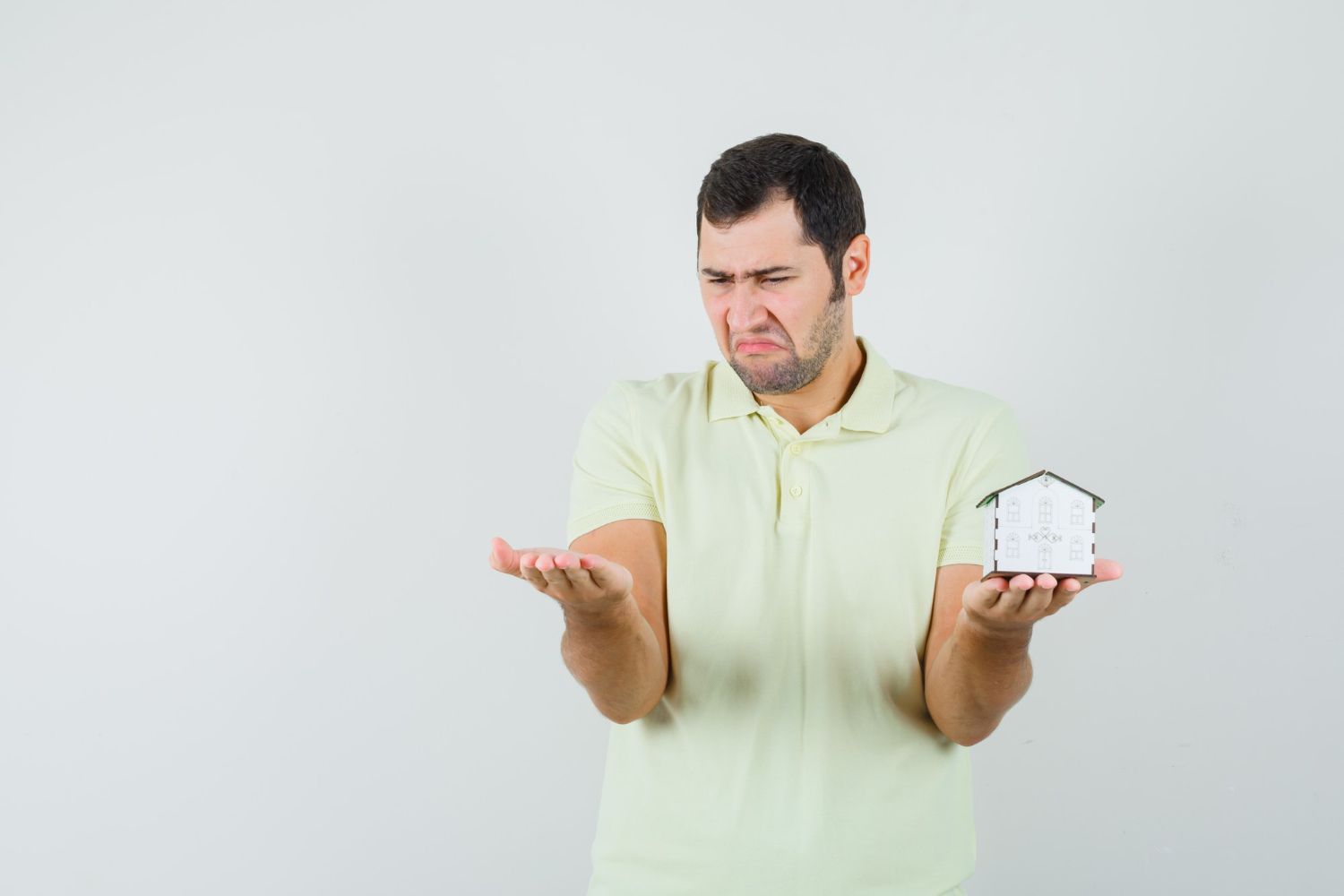 A man is holding a small house in his hands and making a funny face.