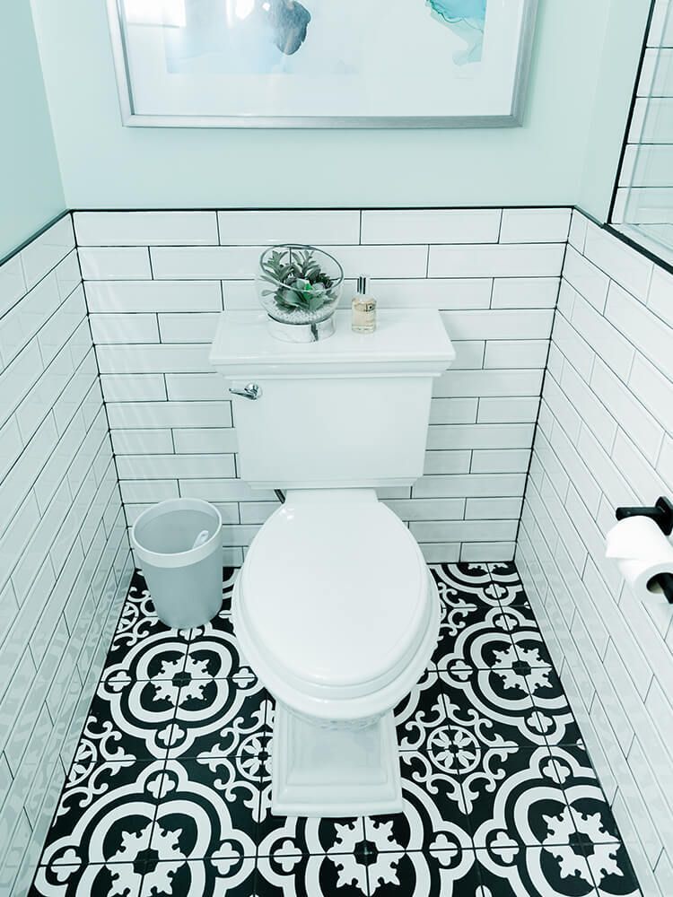 A bathroom with a toilet , trash can , and a picture on the wall.