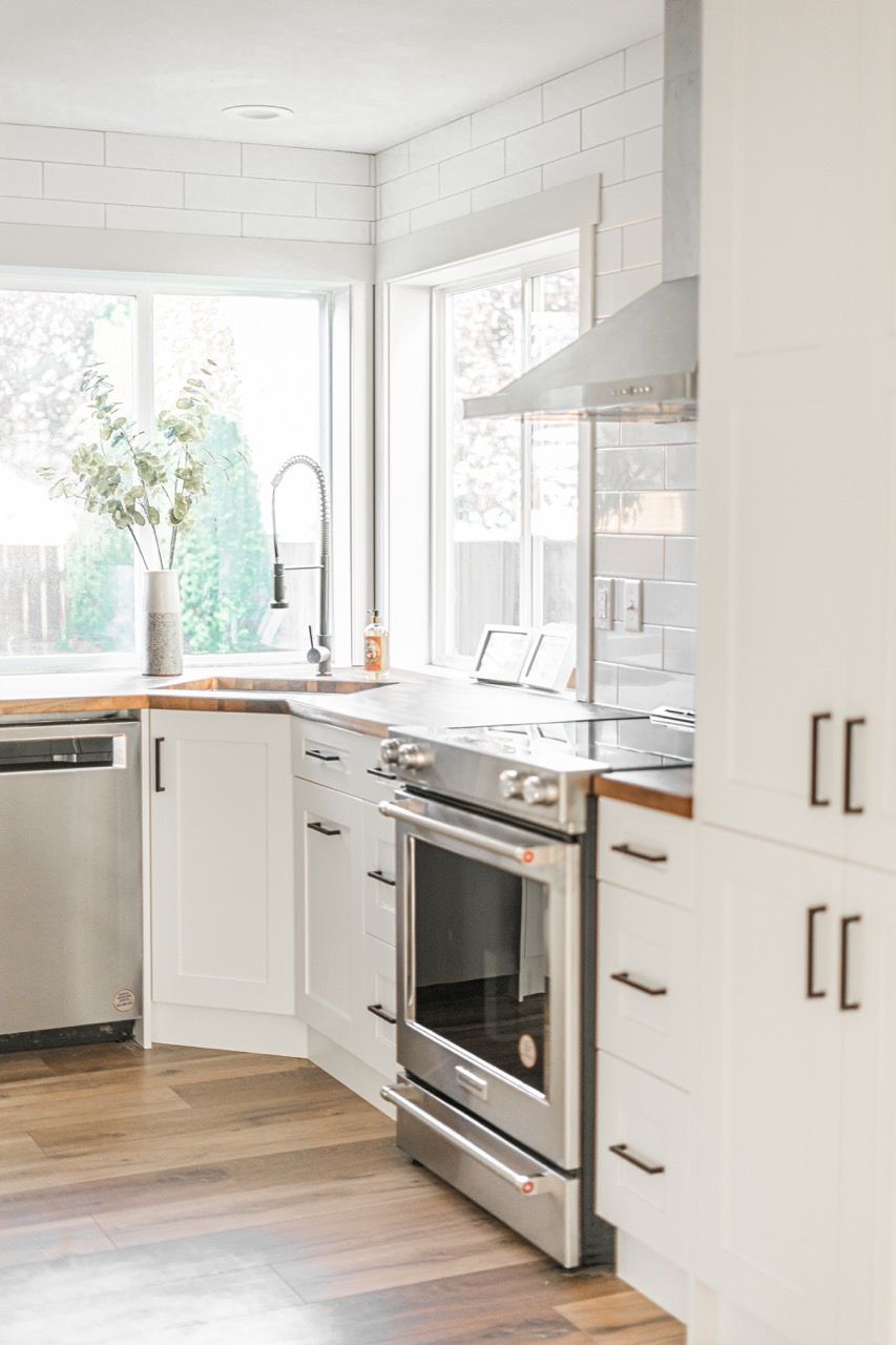 A kitchen with white cabinets , stainless steel appliances , a sink , and a window.