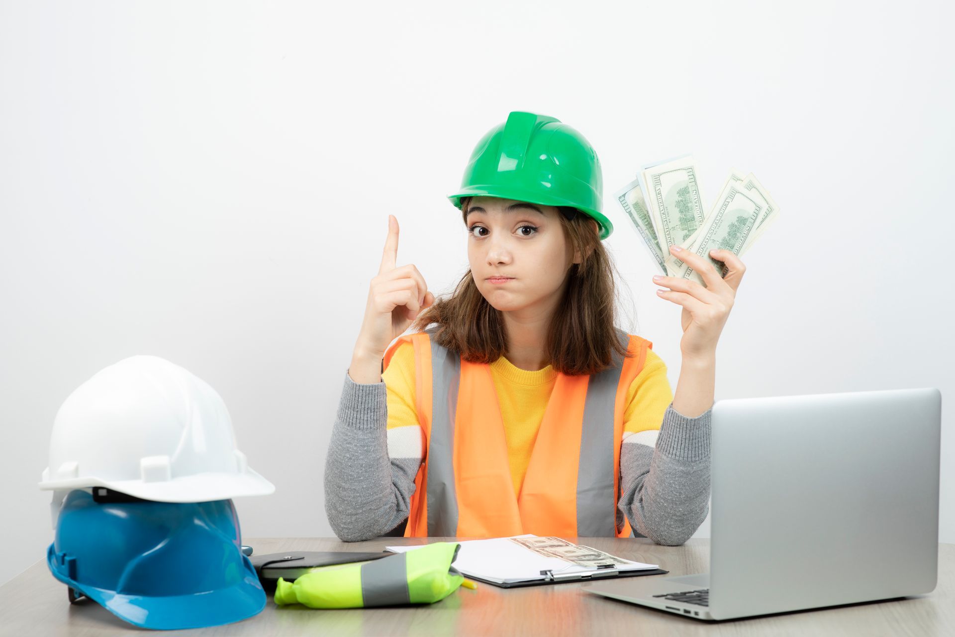 A woman in a hard hat is sitting at a desk holding a bunch of money.