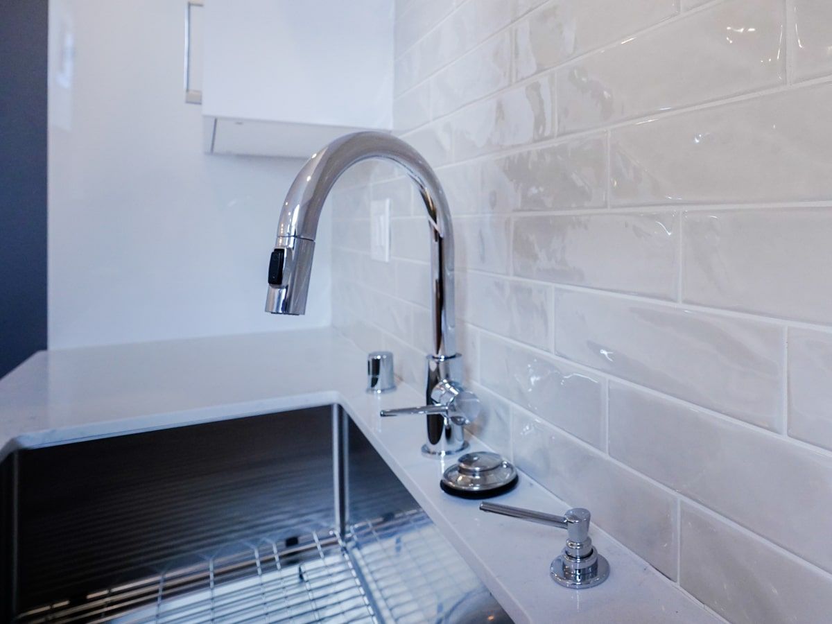 A kitchen sink with a chrome faucet and white tiles.