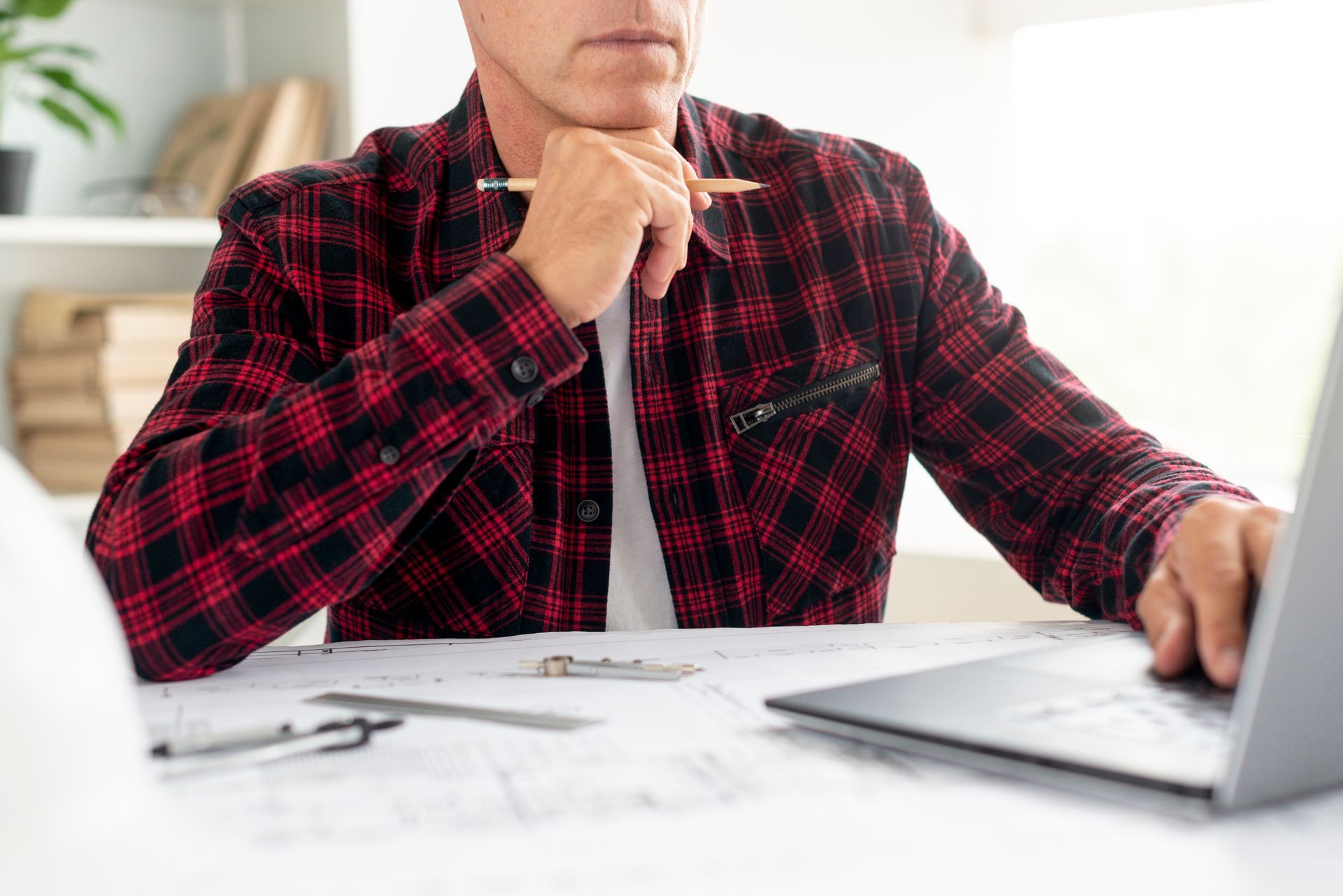 A man in a plaid shirt is sitting at a desk using a laptop computer.