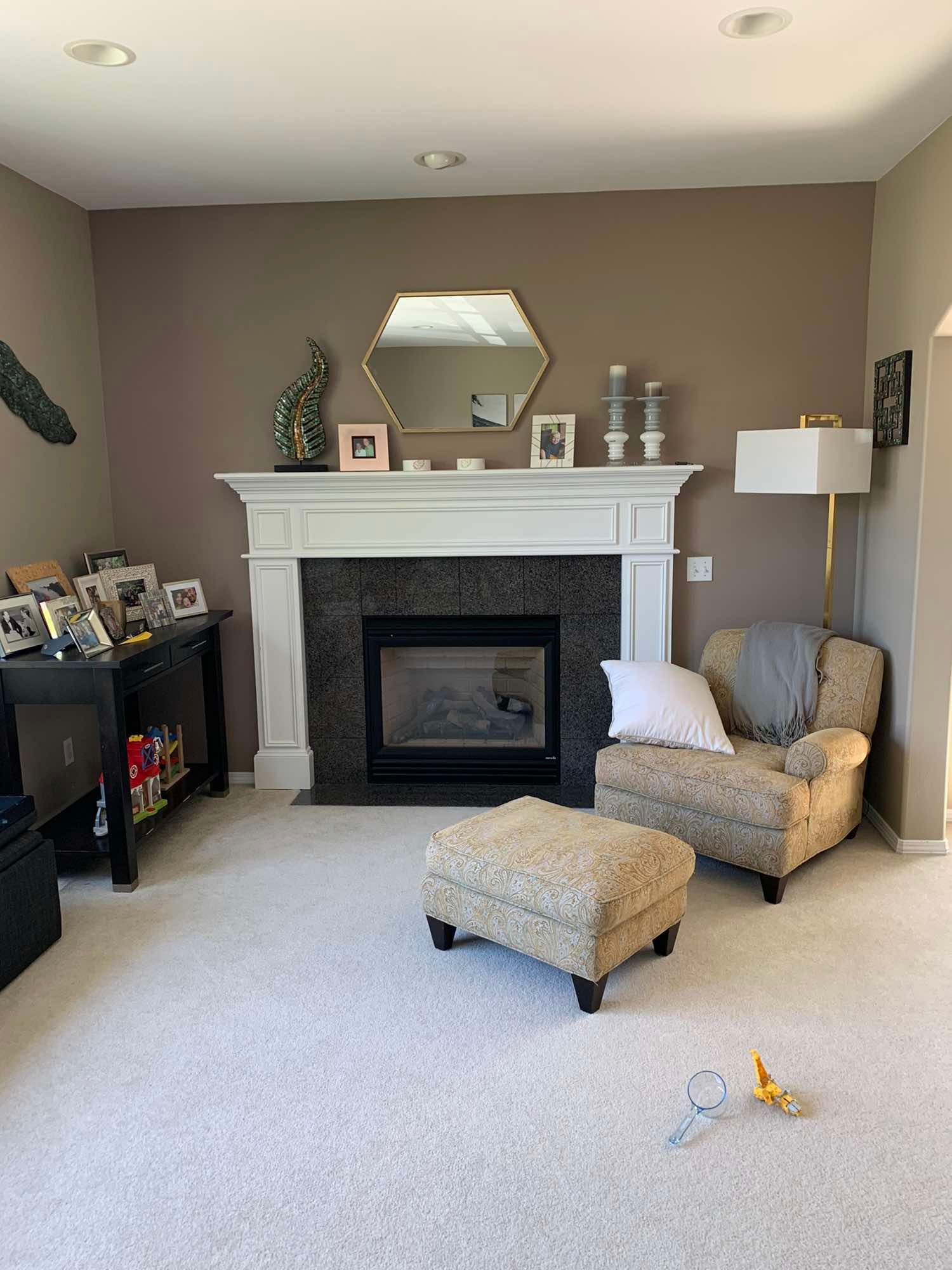 A living room with a fireplace , chair and ottoman.