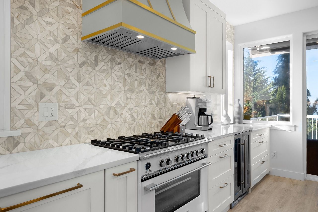 A kitchen with white cabinets , a stove , and a window.