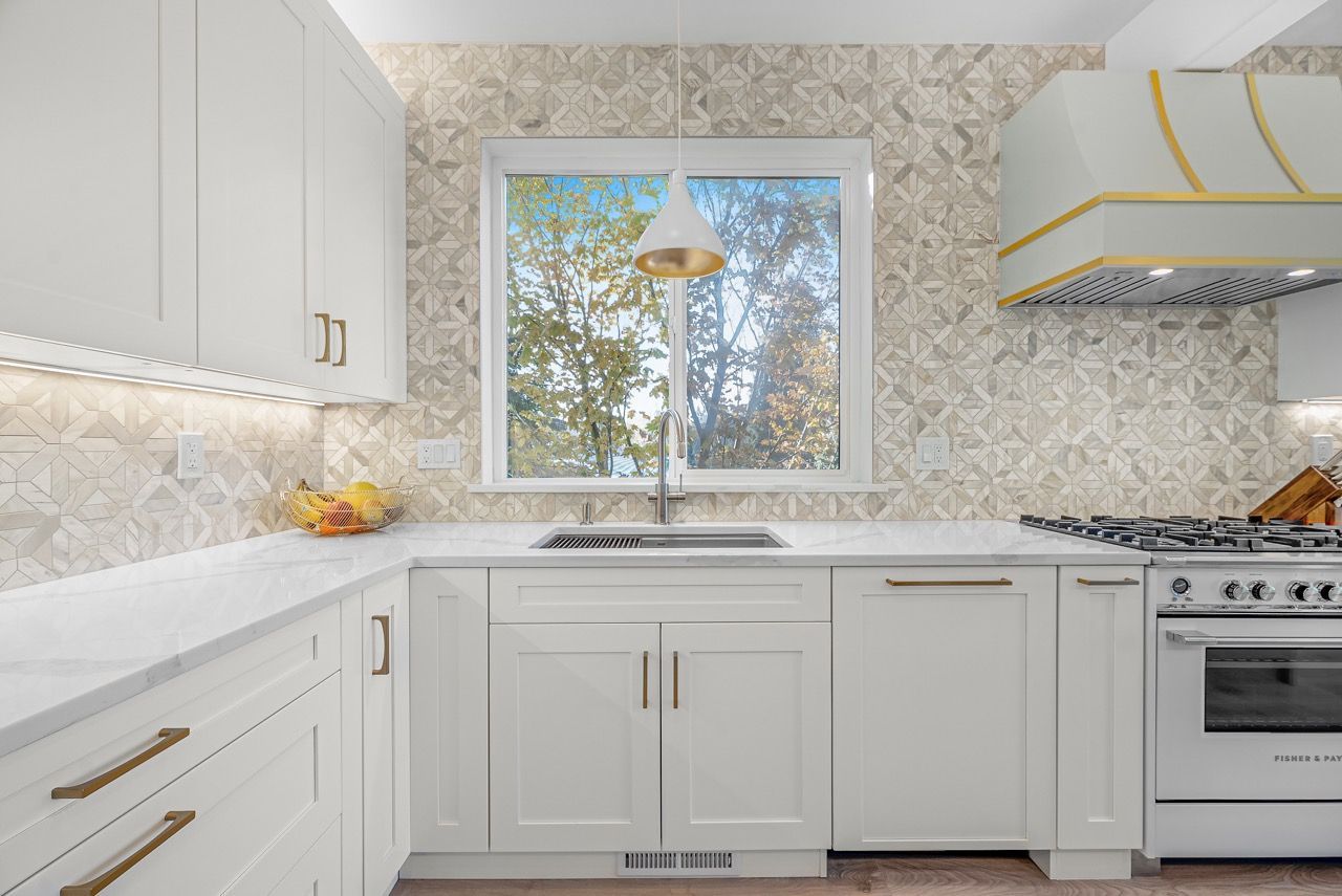 A kitchen with white cabinets , a stove , a sink and a window.