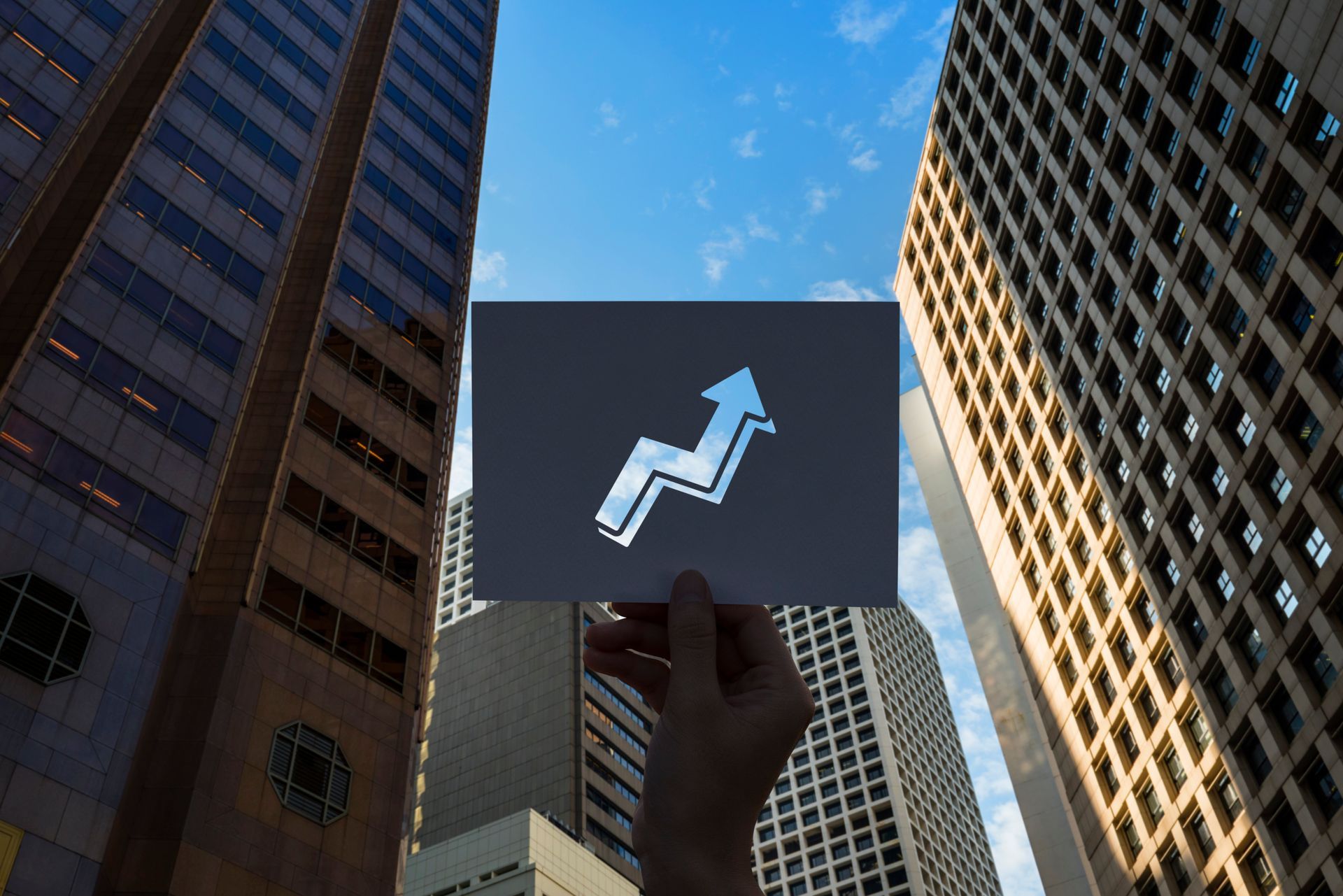 A person is holding a card with an arrow pointing up in front of tall buildings.
