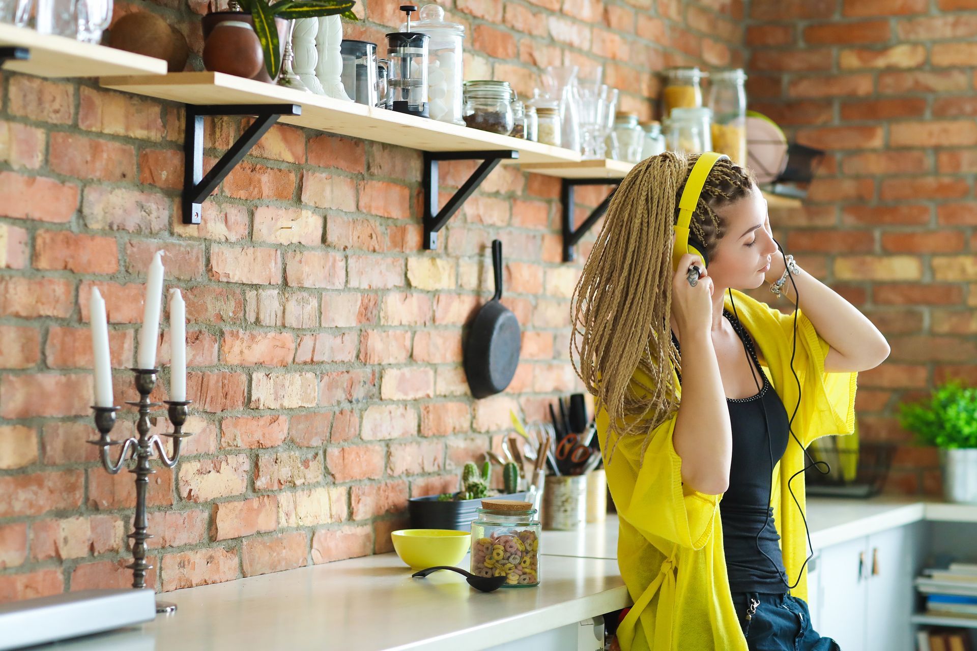 A woman is sitting on a kitchen counter wearing headphones.