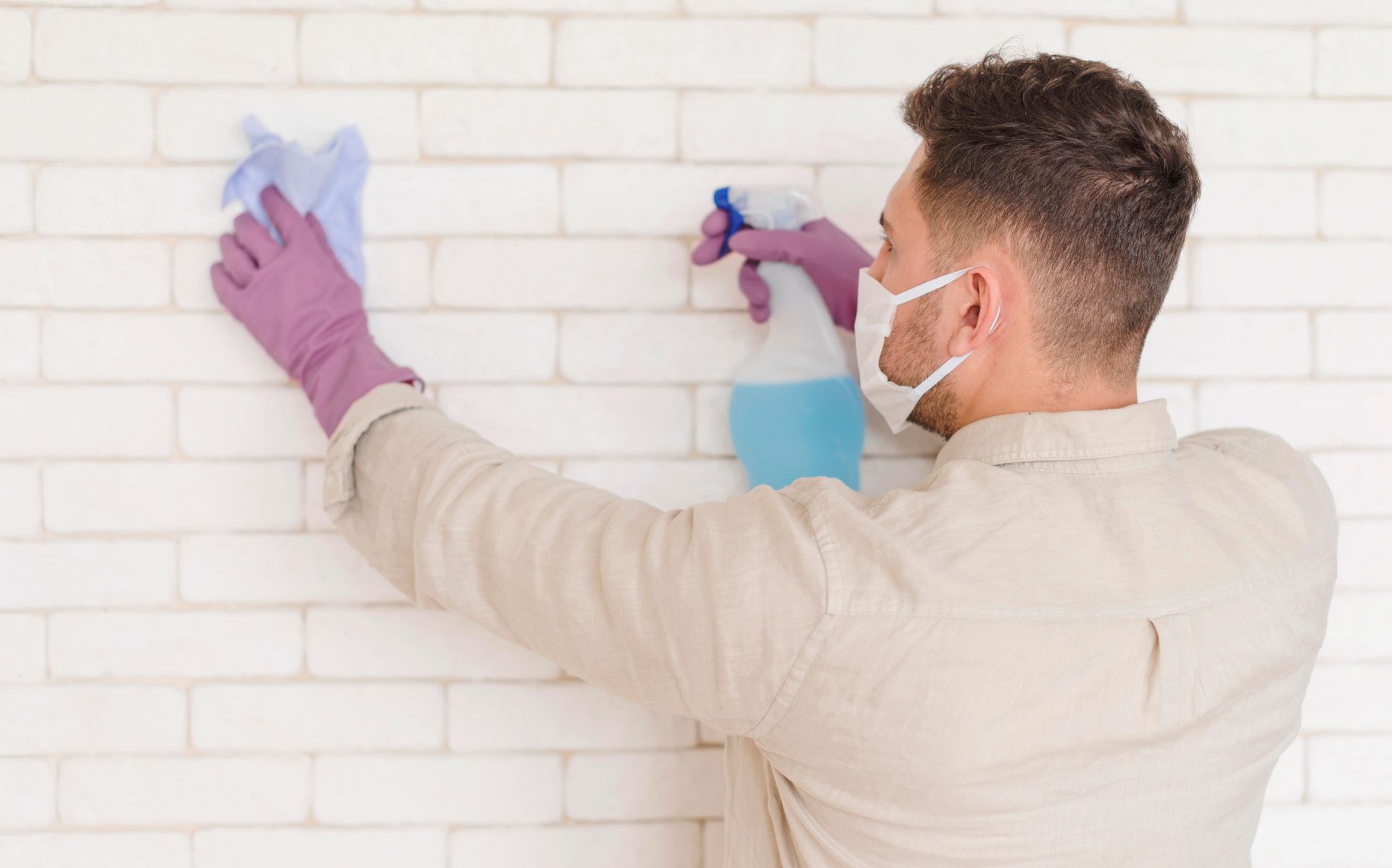 A man wearing a mask and gloves is cleaning a brick wall.