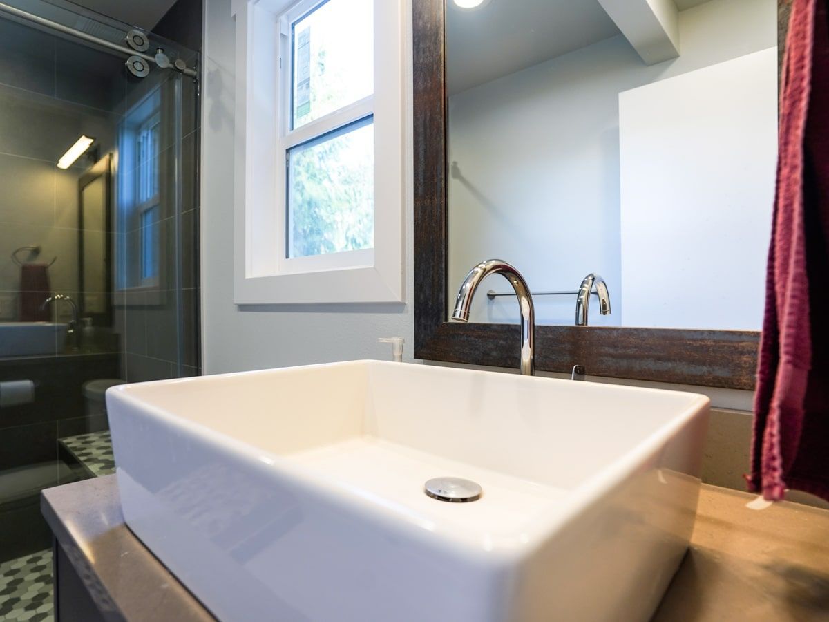 A bathroom with a sink , mirror and window.
