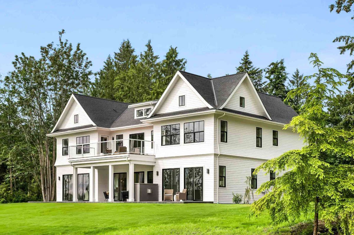A large white house with a black roof is sitting on top of a lush green field.