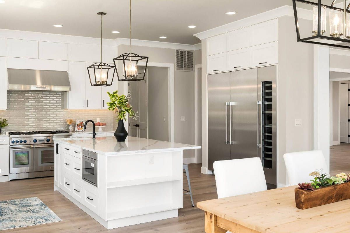 A kitchen with white cabinets , stainless steel appliances , a wooden table and chairs.