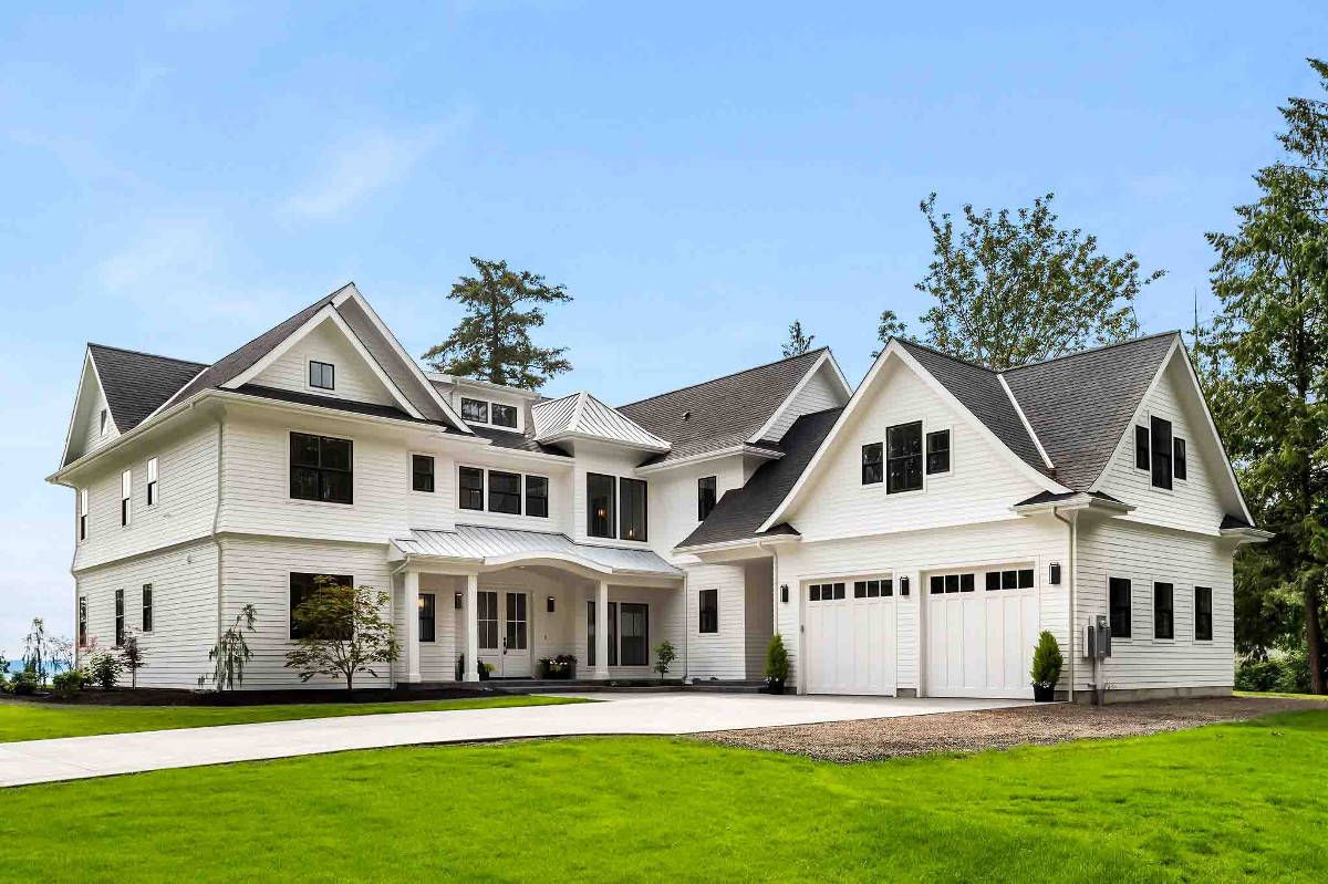 A large white house with a black roof is sitting on top of a lush green field.