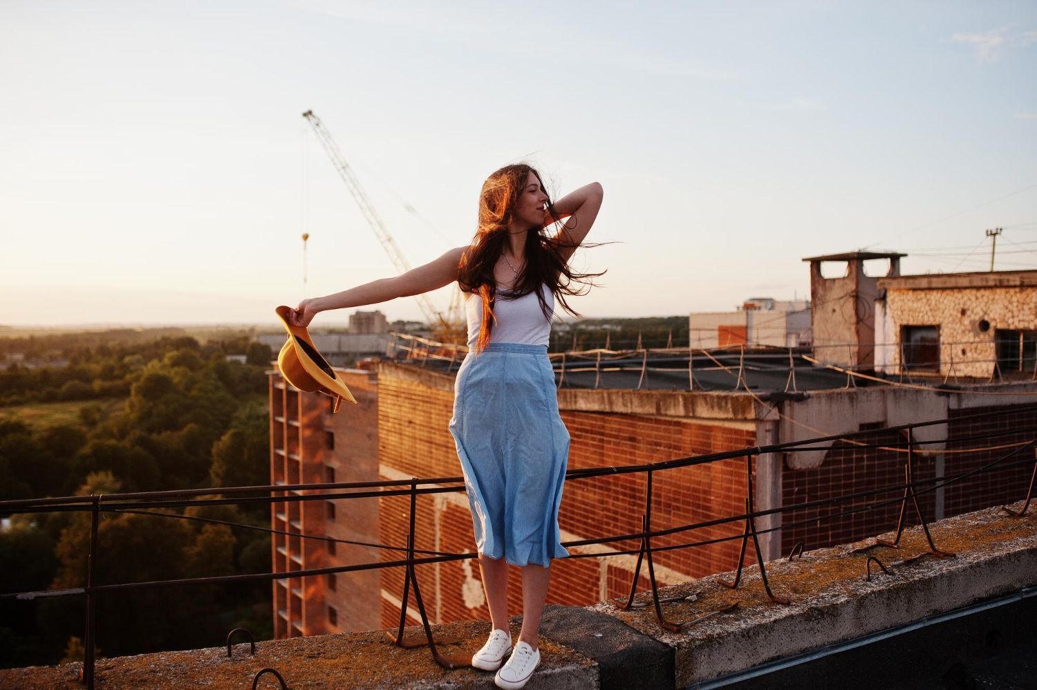 A woman is standing on the roof of a building holding a hat.
