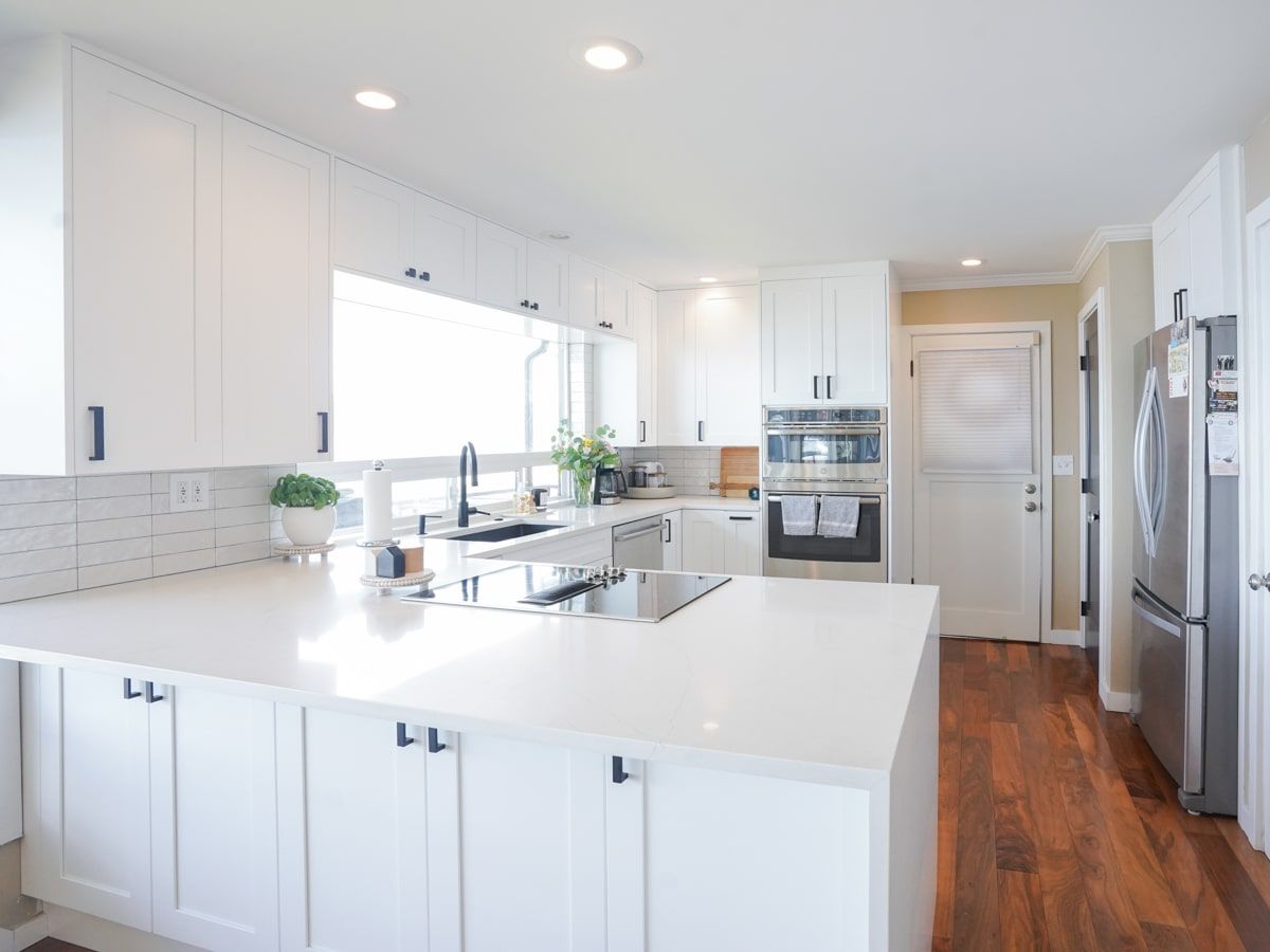 A kitchen with white cabinets , white counter tops , stainless steel appliances and hardwood floors.