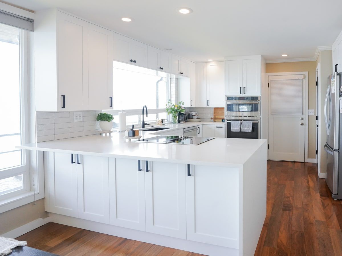 A kitchen with white cabinets , white counter tops , stainless steel appliances and hardwood floors.
