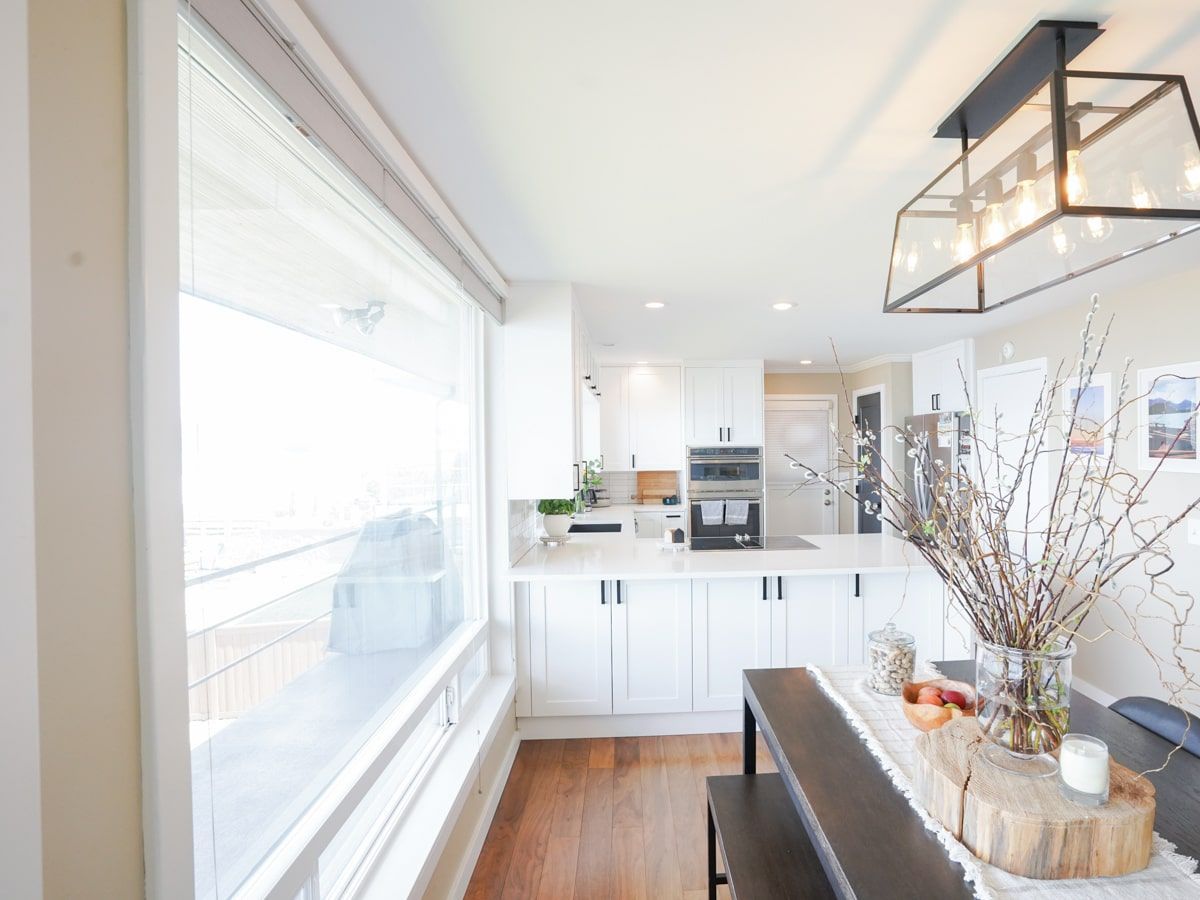A kitchen with white cabinets , wooden floors and a large window.