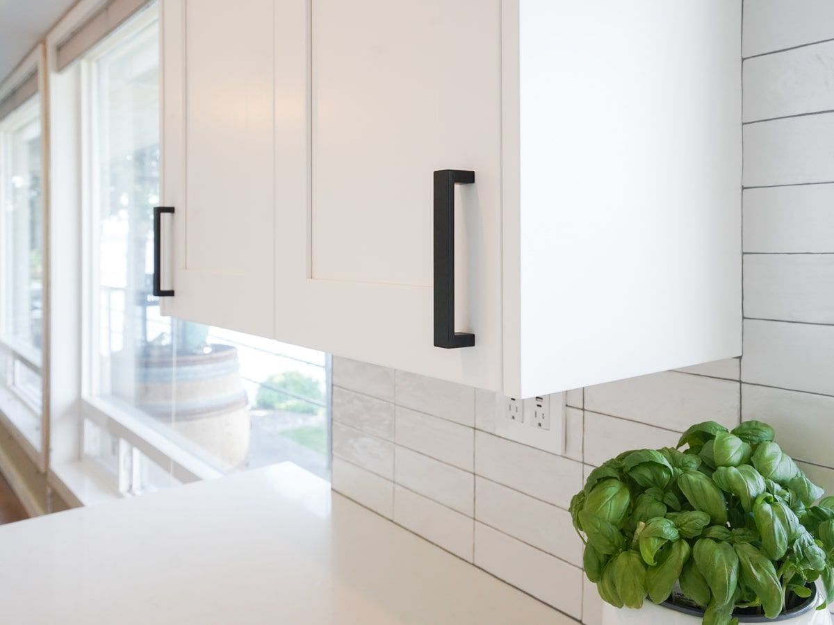 A kitchen with white cabinets and black handles