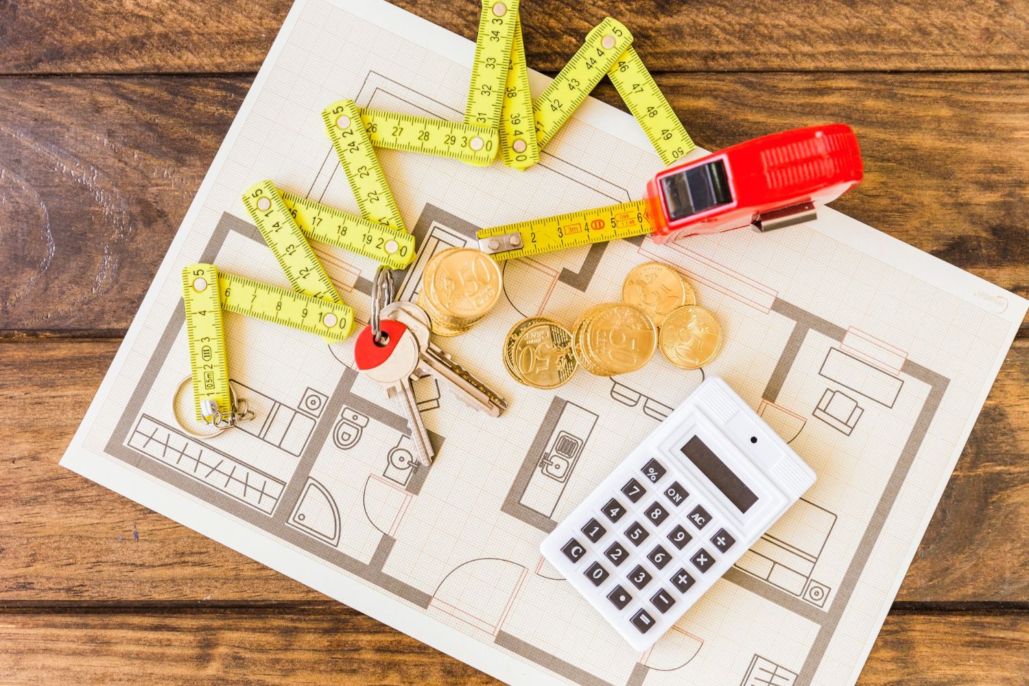 A calculator , measuring tape , keys and coins are on a house plan.