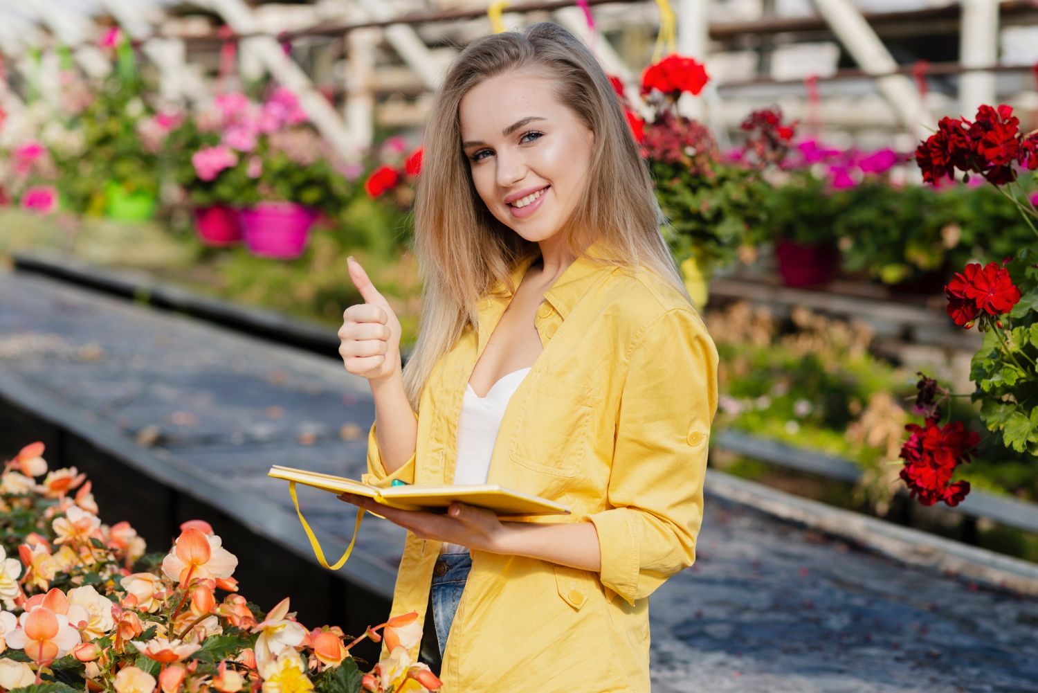 A woman in a yellow shirt is holding a notebook and giving a thumbs up.