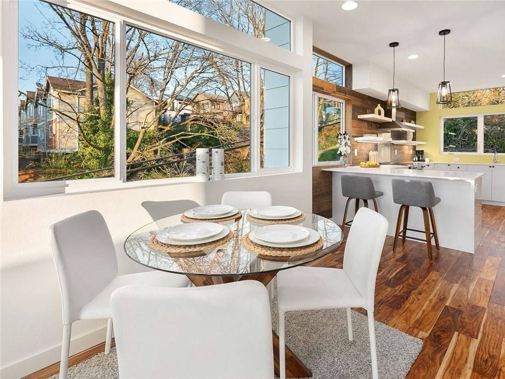 A dining room with a glass table and white chairs and a large window.