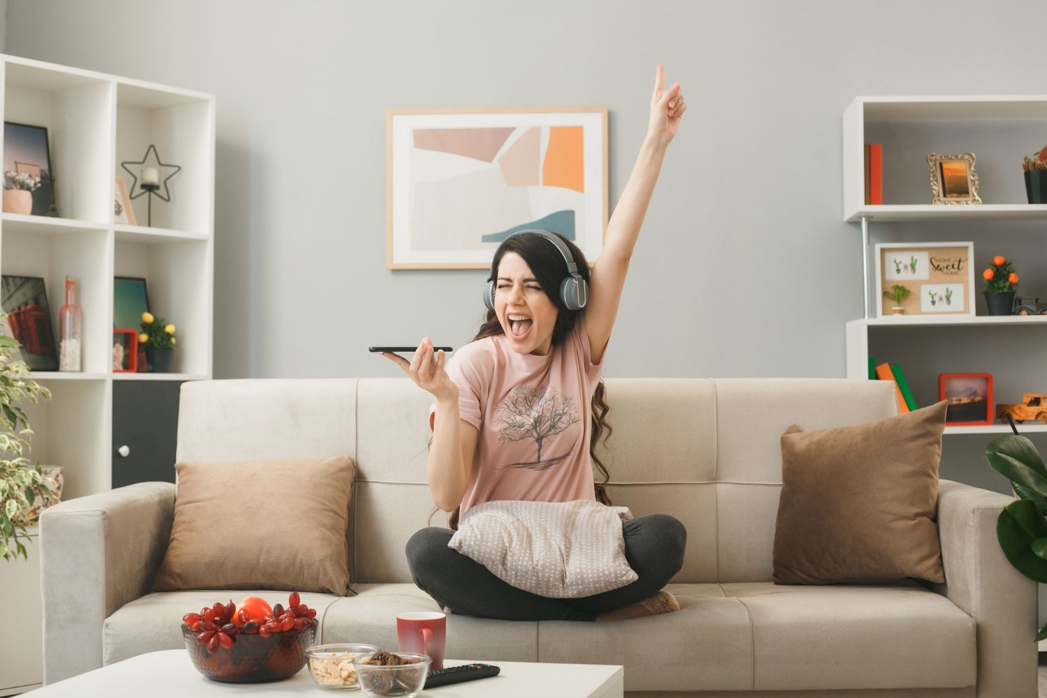 A woman is sitting on a couch wearing headphones and holding a remote control.