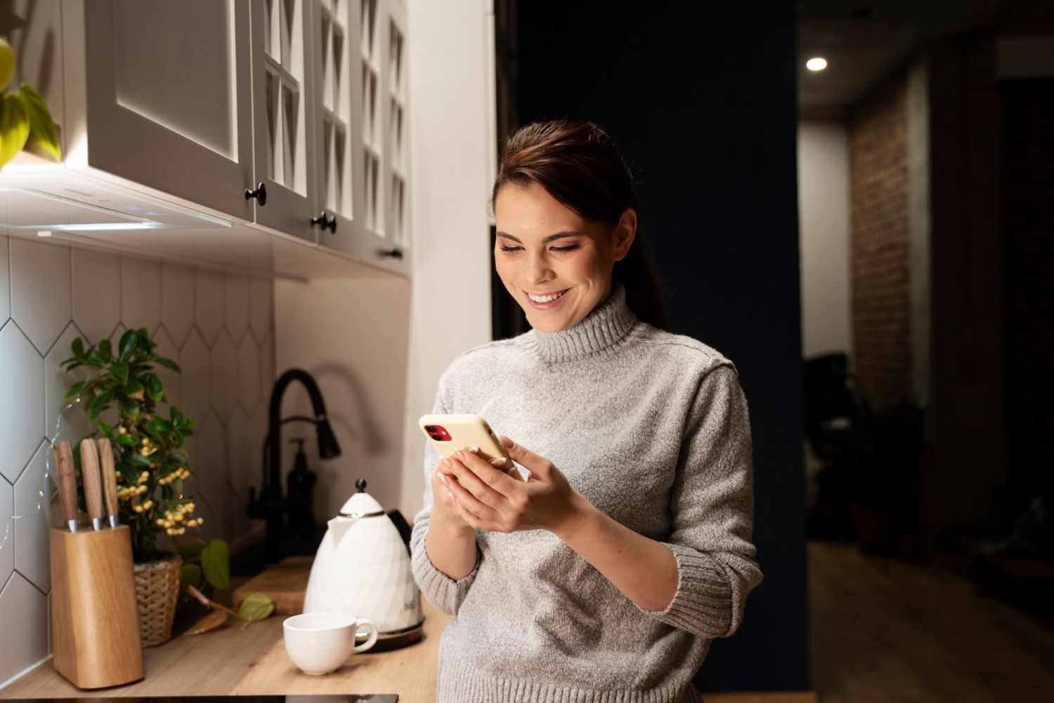 A woman is standing in a kitchen looking at her cell phone.