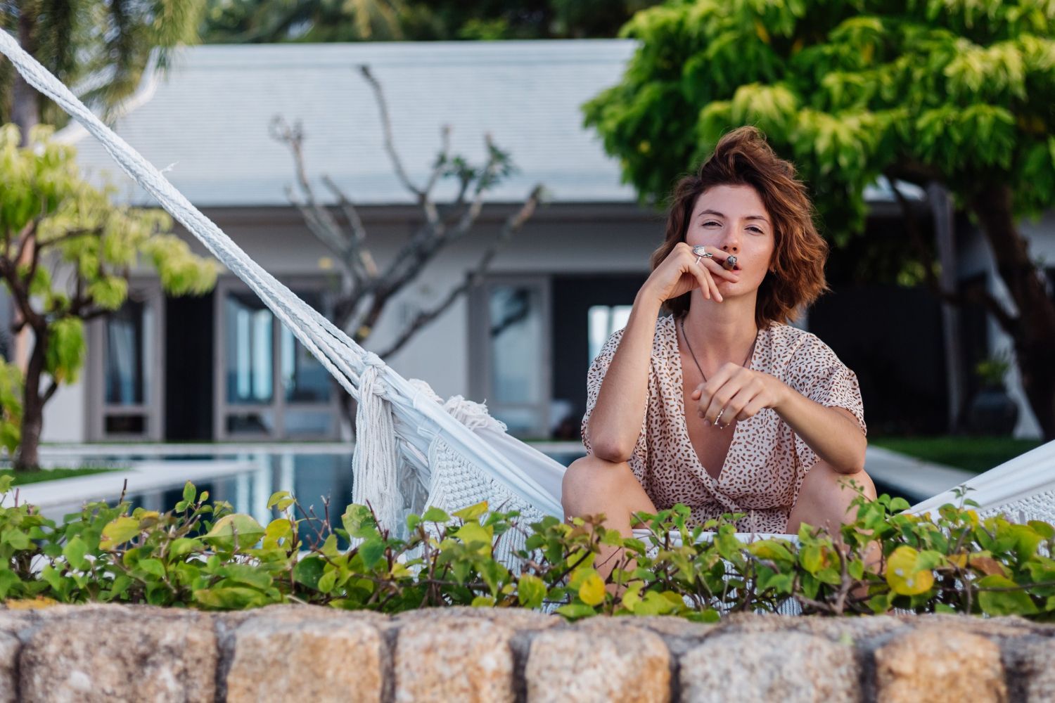 A woman is sitting in a hammock in front of a house.