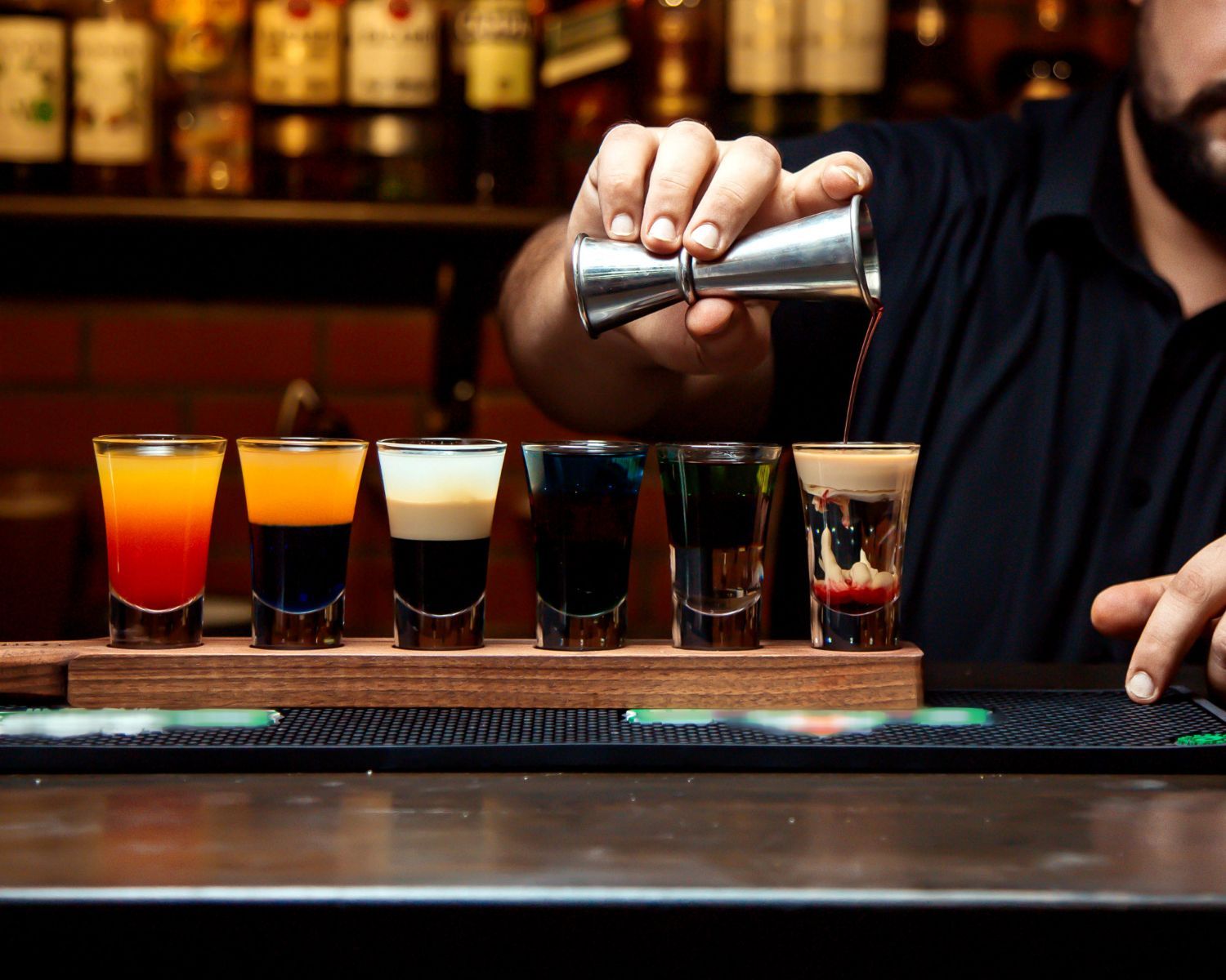 A bartender is pouring a drink into a shot glass.