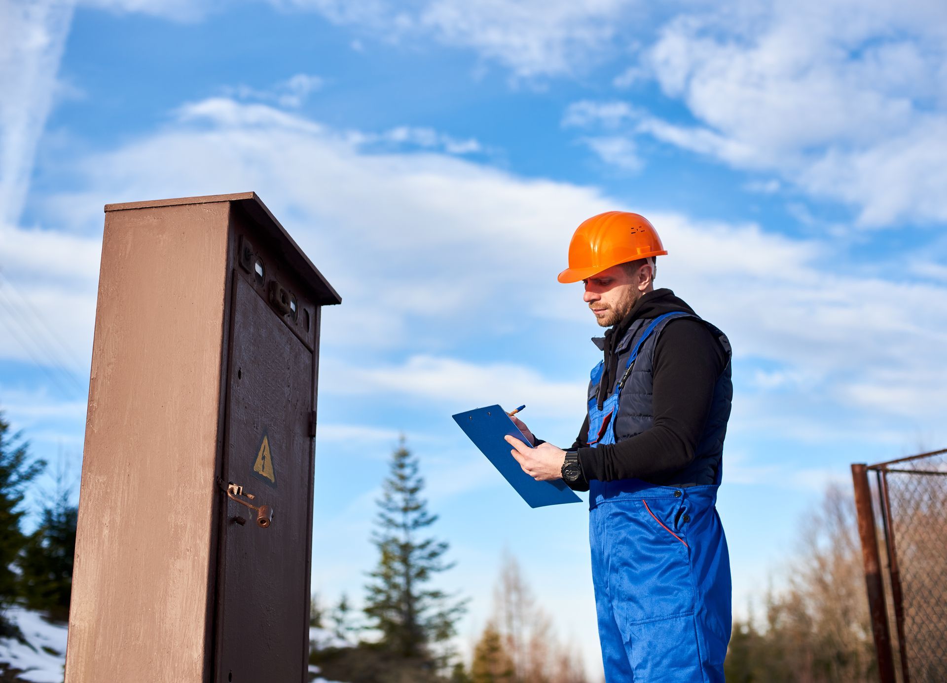 A man in a hard hat is holding a clipboard and writing on it.