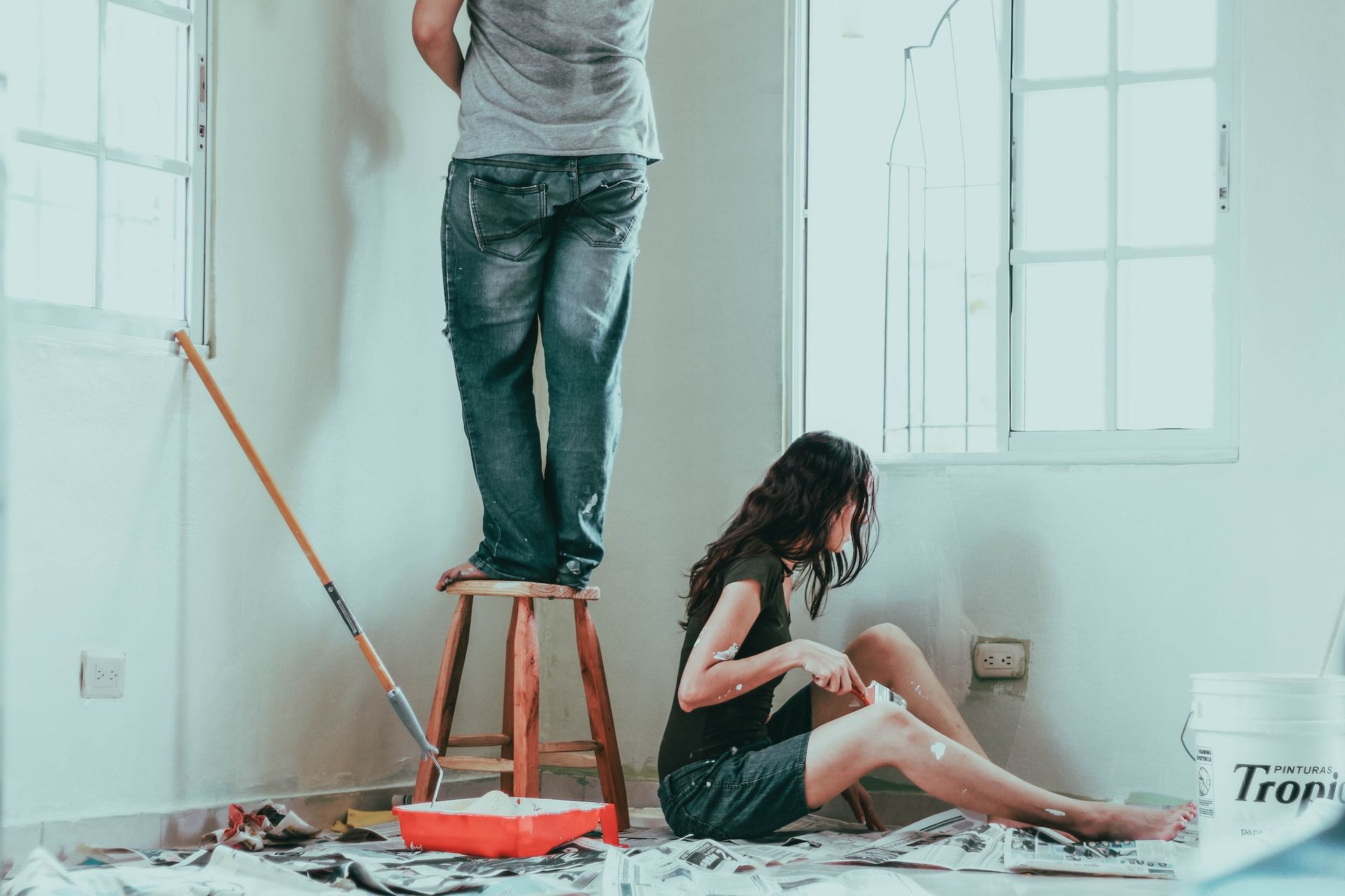 A man is standing on a stool while a woman sits on the floor.