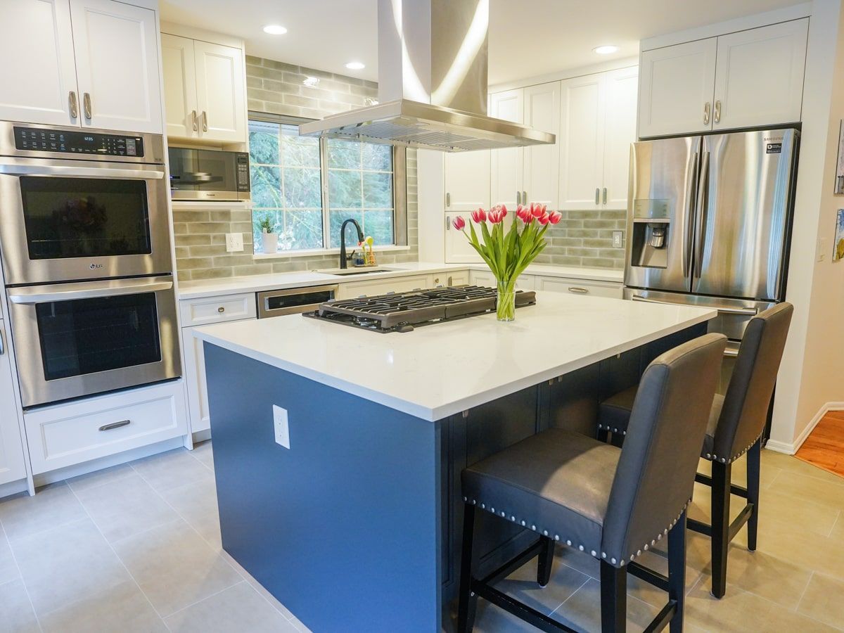 A kitchen with white cabinets , stainless steel appliances , a large island and a vase of flowers on the counter.