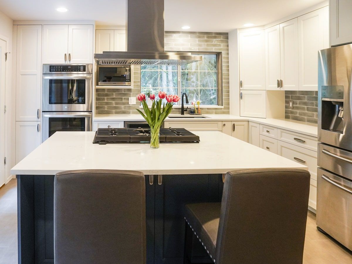 A kitchen with white cabinets and stainless steel appliances and a large island with a vase of flowers on it.