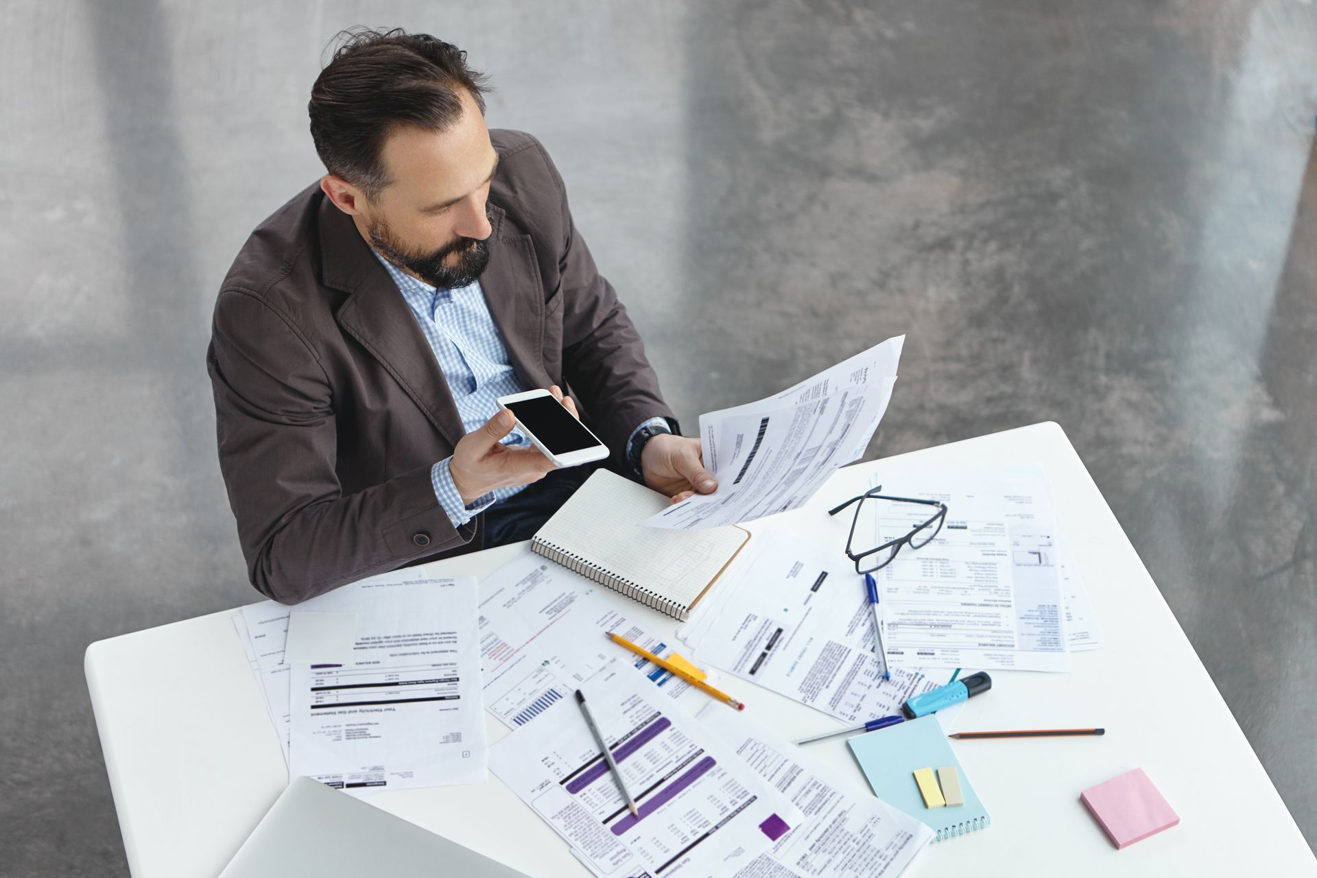 A man is sitting at a desk with papers and a cell phone.