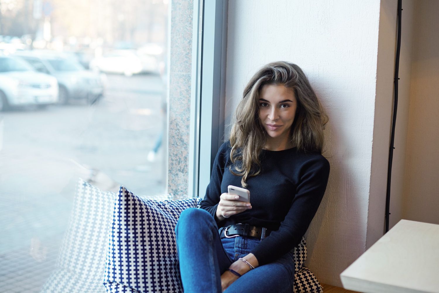 A woman is sitting on a window sill looking at her phone.