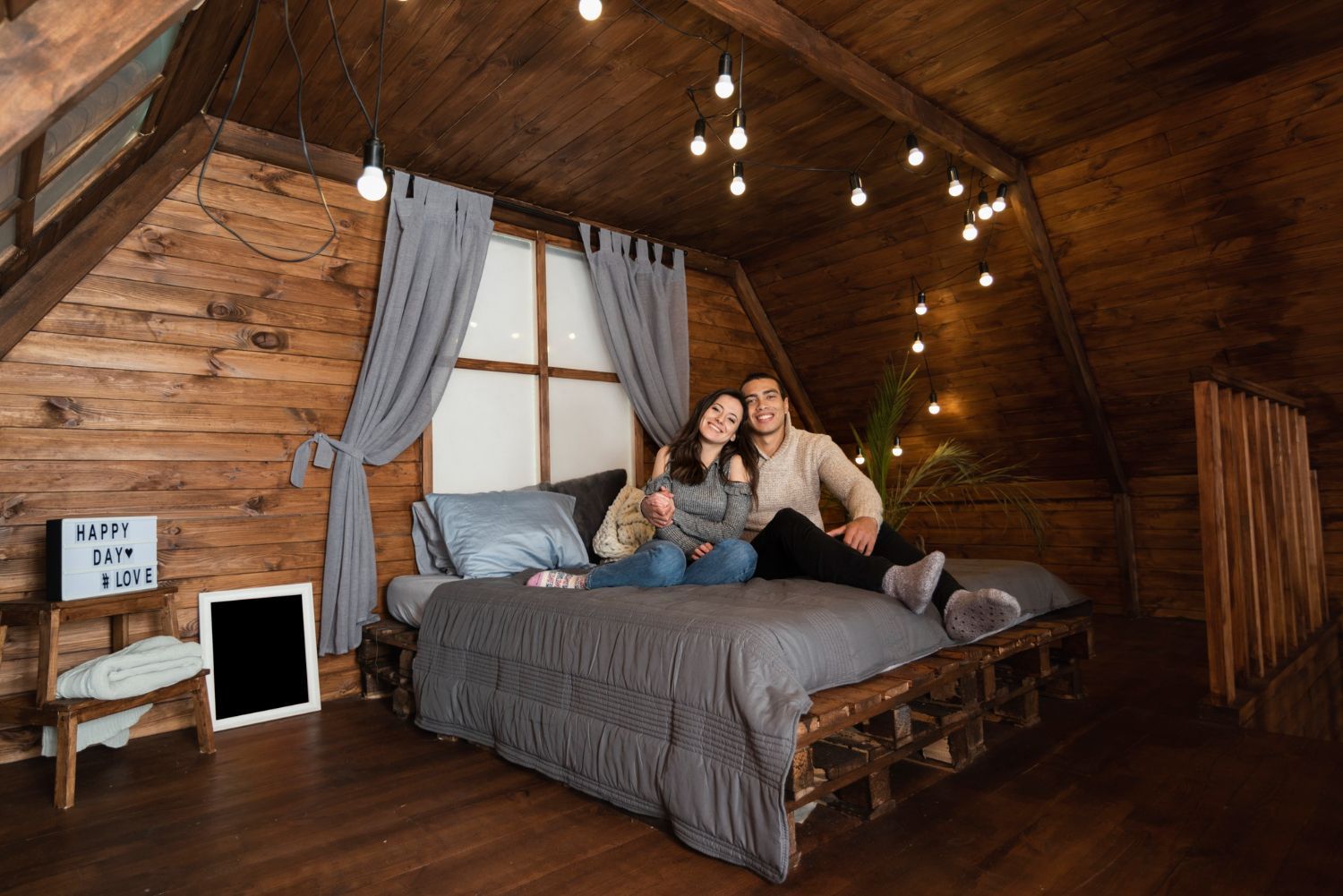 A man and a woman are sitting on a bed in a wooden room.