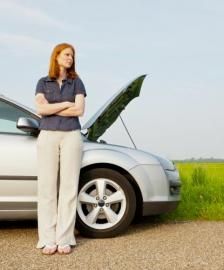 Person standing beside a silver car with its hood open on a roadside.