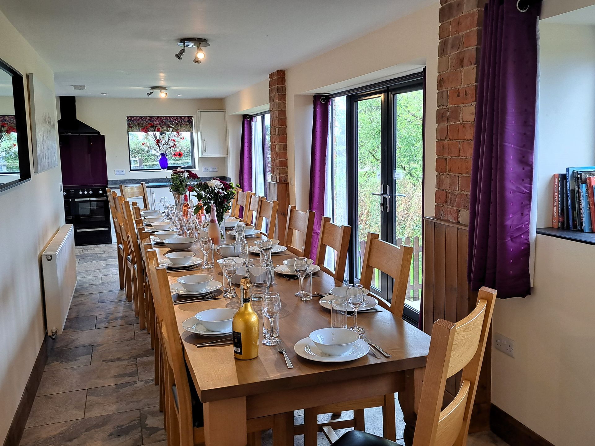 Long dining table, laid for a meal with flowers and wine and large windows