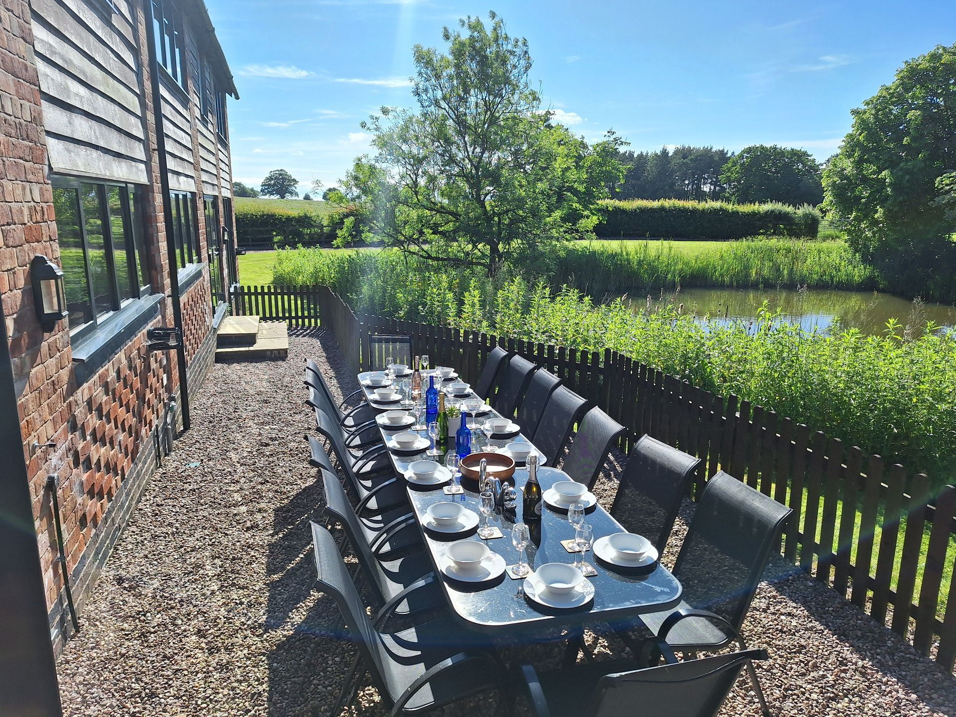 Patio table laid with crockery and wine glasses over looking a wildlife pond next to a barn