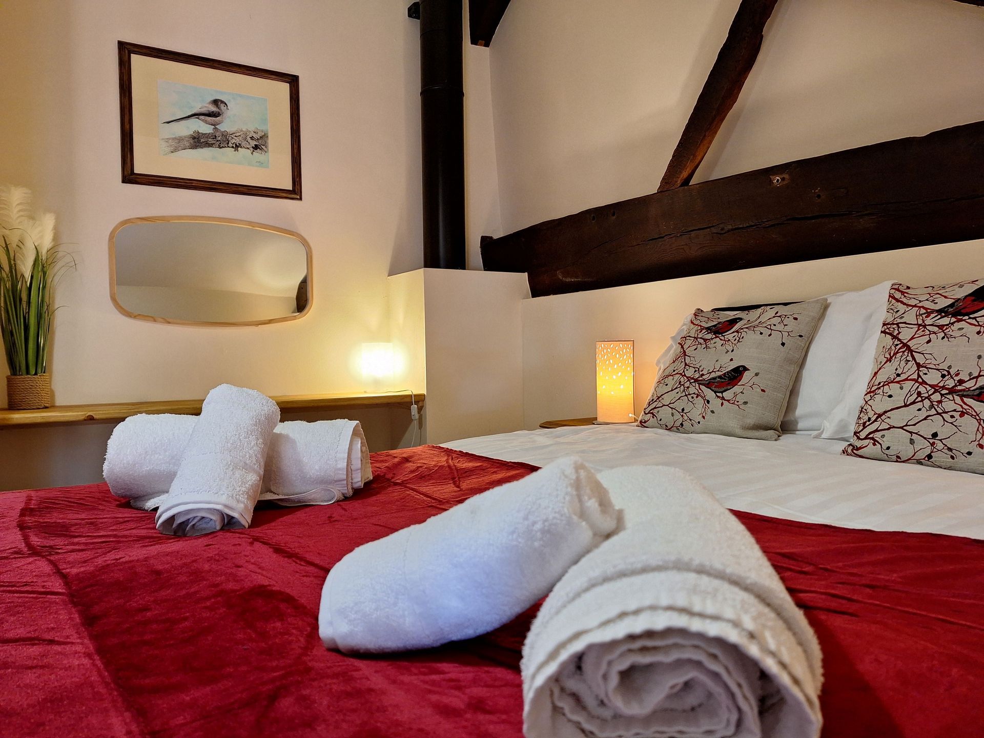 Double bedroom with rolled white towels and bedside lamps and beams