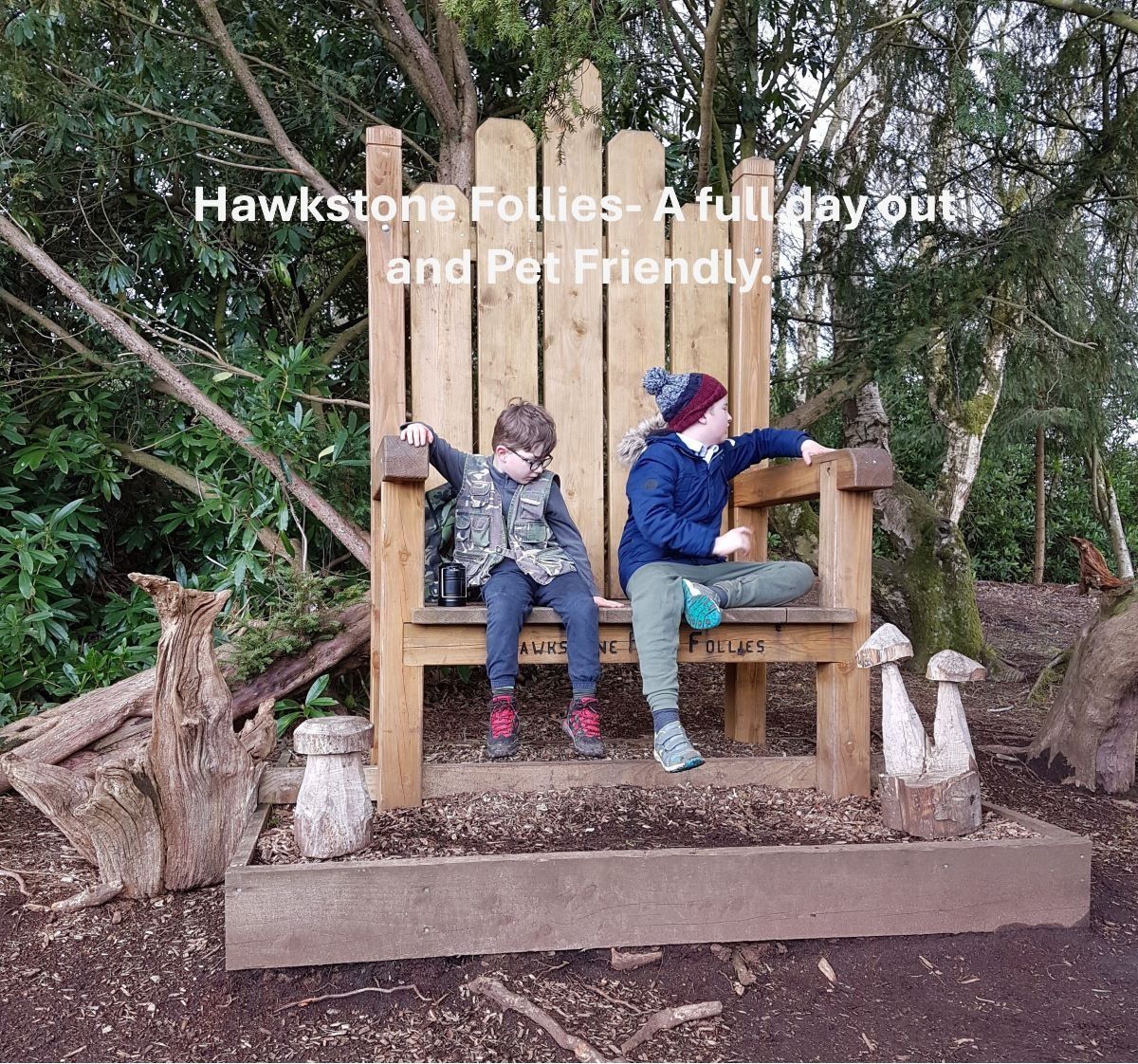 two small boys sitting on a giant wooden chair with a tree behind them