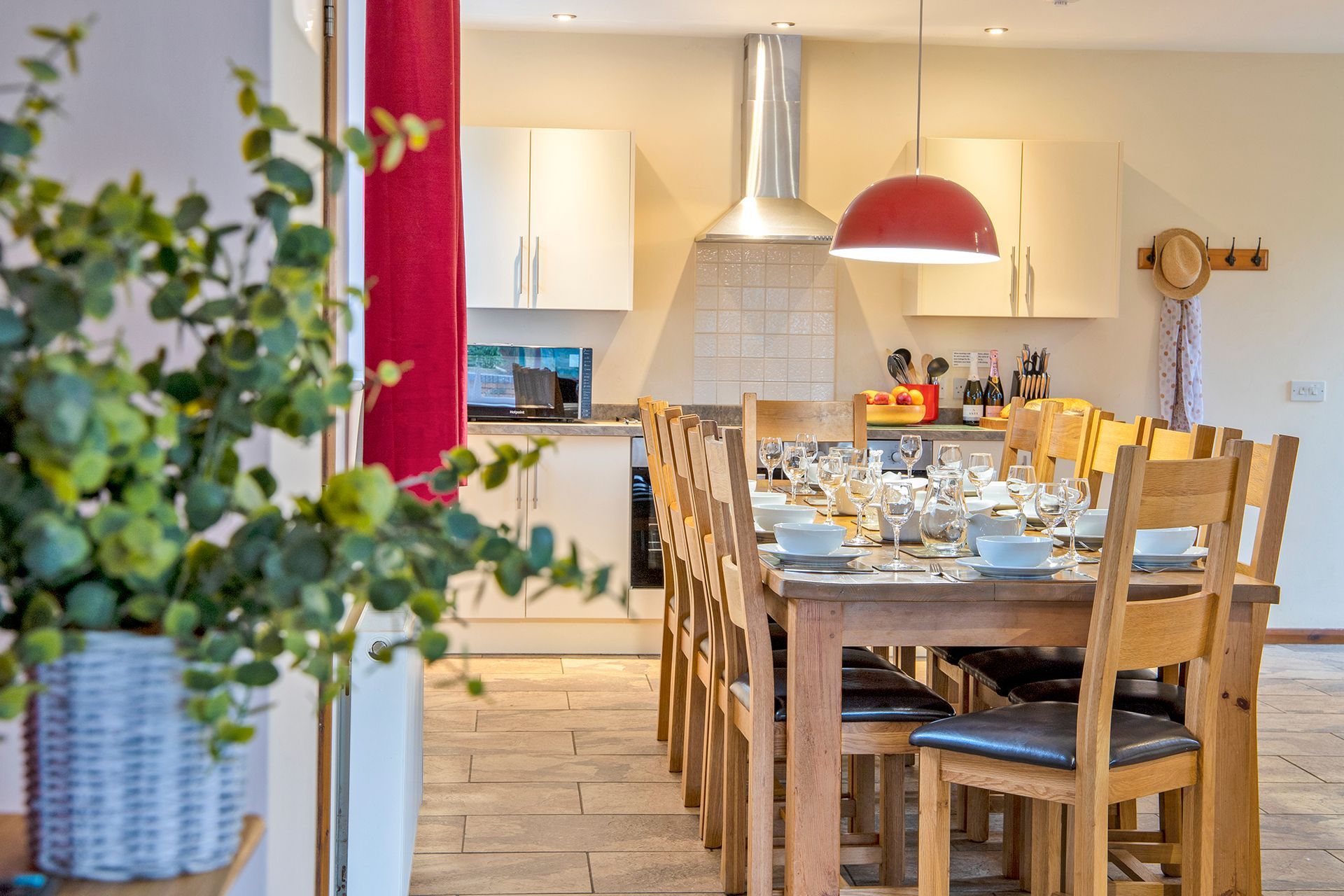 Large dining table laid with white china and wine glasses, with dining chairs  and a red lamp