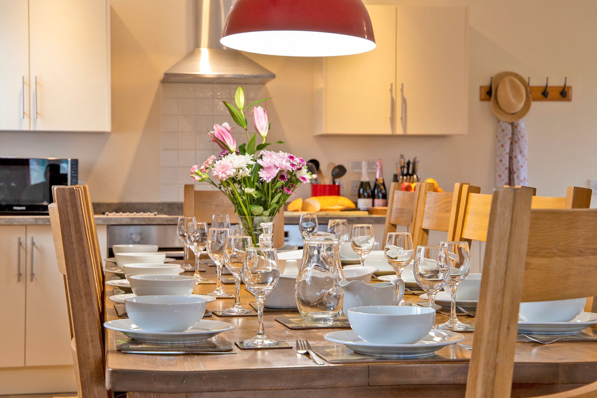 Laid dining table with vase of pink flowers and red lamp over the table