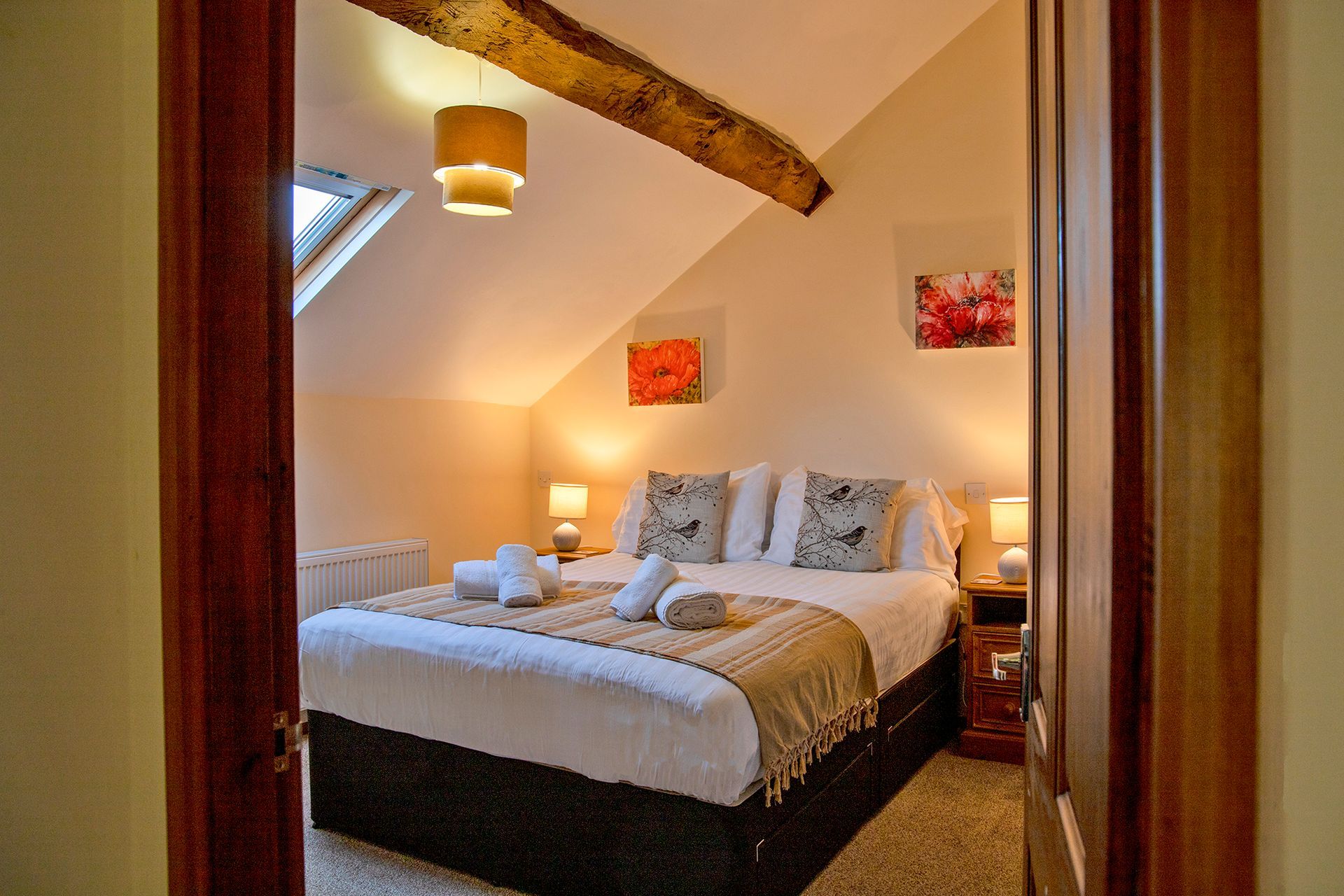 A king size bed made with white linen and folded cushions. Looking through an open door